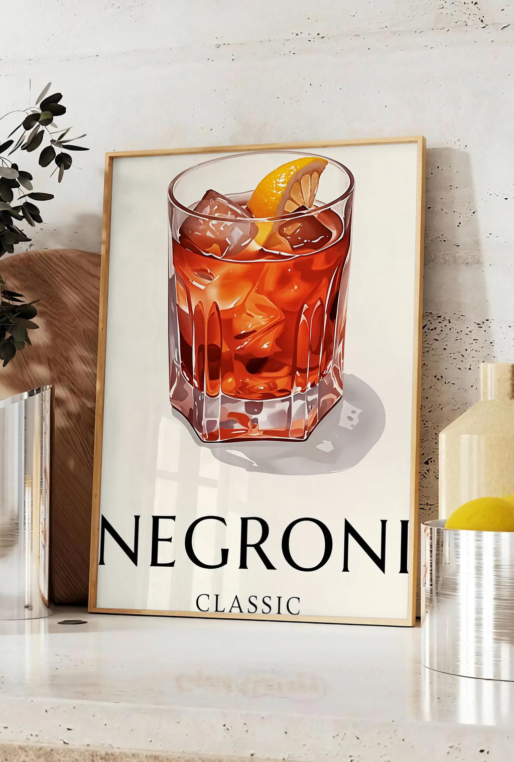 Affiche affiche cocktail Negroni, posee sur un plan de travail de cuisine en pierre claire, entre une branche d'eucalyptus en vase et un bocal de citrons