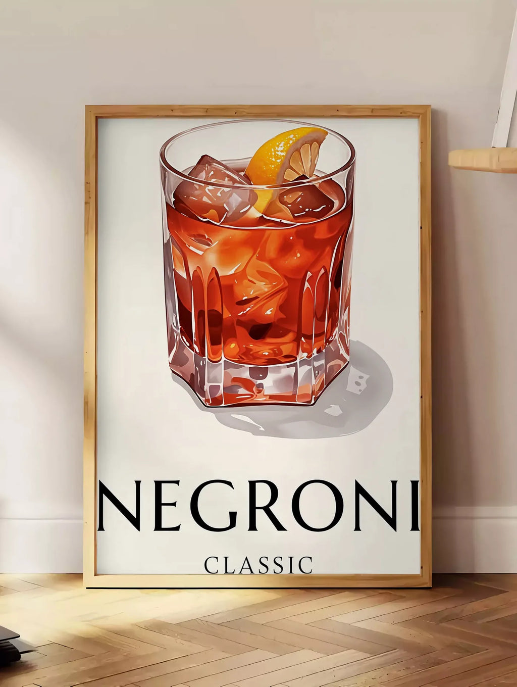 Estampe affiche cocktail Negroni, posee au sol dans un coin salon, sur un parquet a chevrons, pres d'une table d'appoint en chene chargee de livres