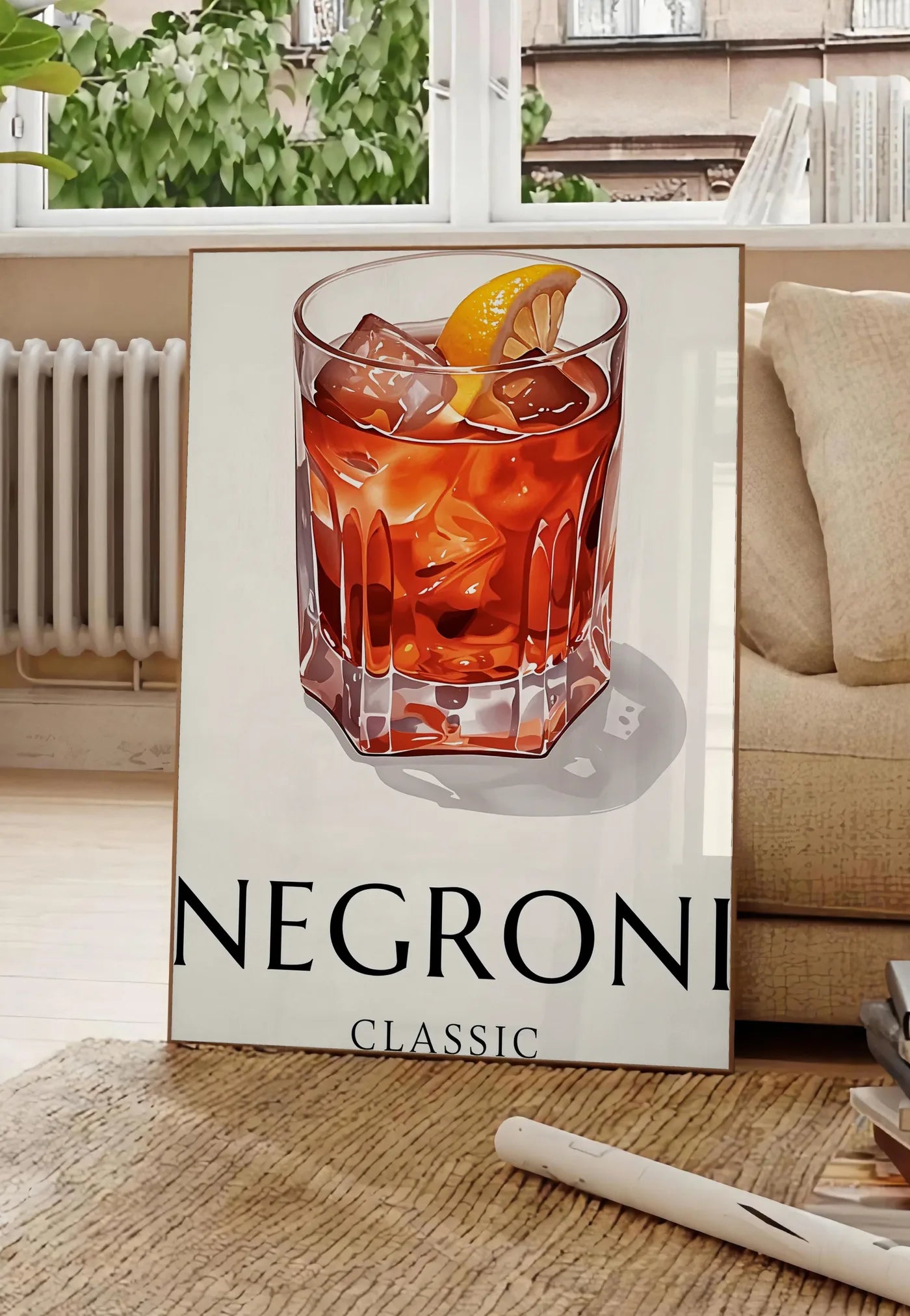 Poster affiche cocktail Negroni, posee au sol dans un salon parisien, devant une grande fenetre donnant sur un immeuble haussmannien, entre un ficus et un canape creme
