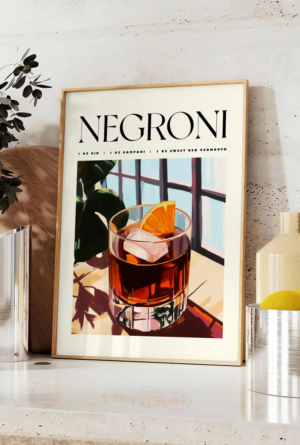 Affiche affiche cocktail Negroni, posee sur un plan de travail de cuisine en pierre claire, entre une branche d'eucalyptus en vase et un bocal de citrons