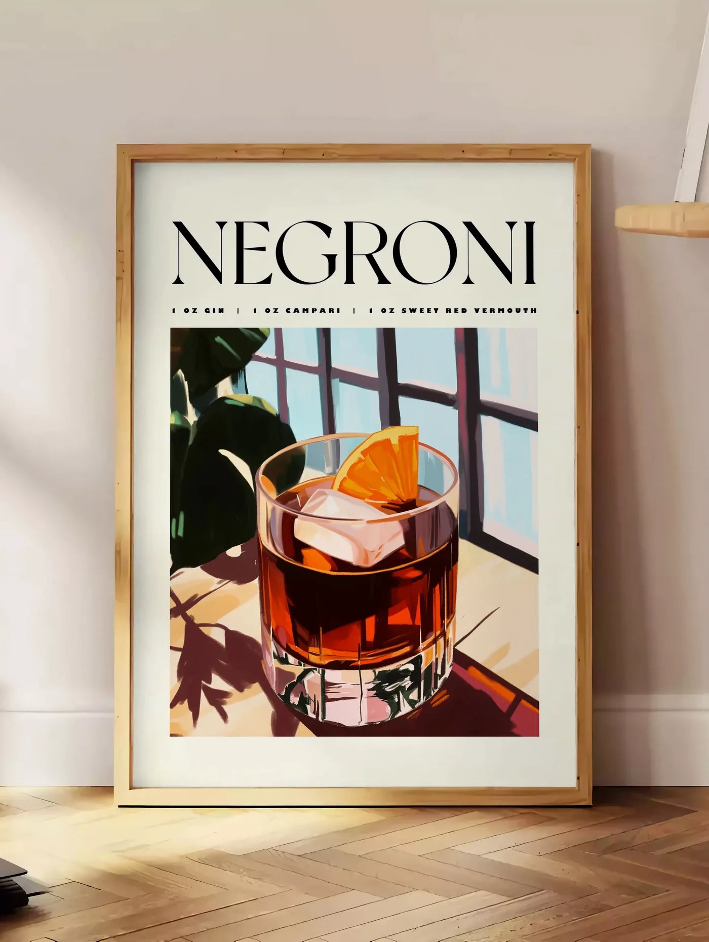 Estampe affiche cocktail Negroni, posee au sol dans un coin salon, sur un parquet a chevrons, pres d'une table d'appoint en chene chargee de livres