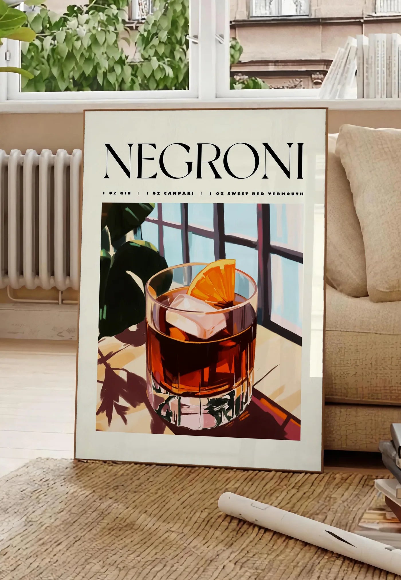 Poster affiche cocktail Negroni, posee au sol dans un salon parisien, devant une grande fenetre donnant sur un immeuble haussmannien, entre un ficus et un canape creme