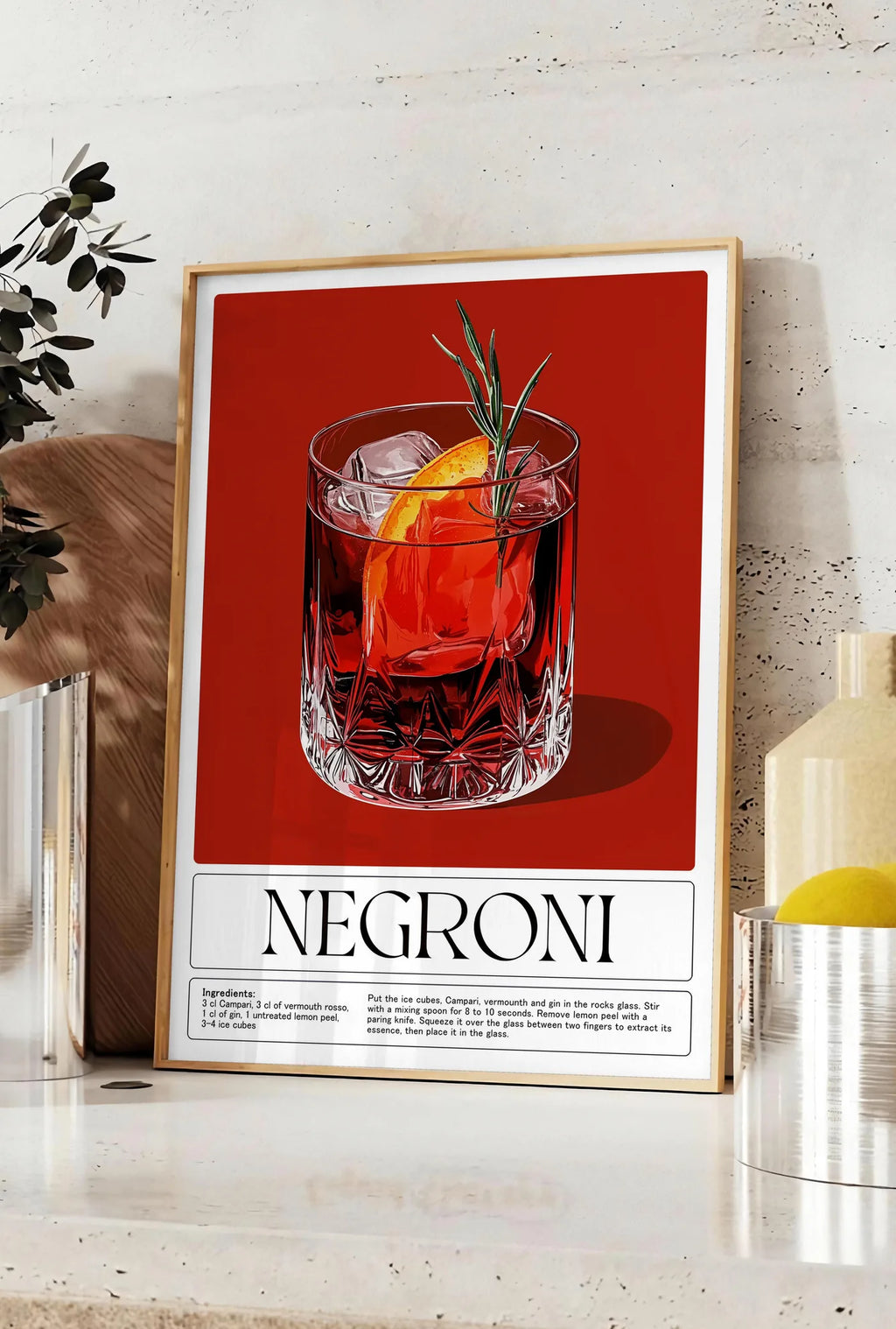 Affiche affiche cocktail Negroni, posee sur un plan de travail de cuisine en pierre claire, entre une branche d'eucalyptus en vase et un bocal de citrons