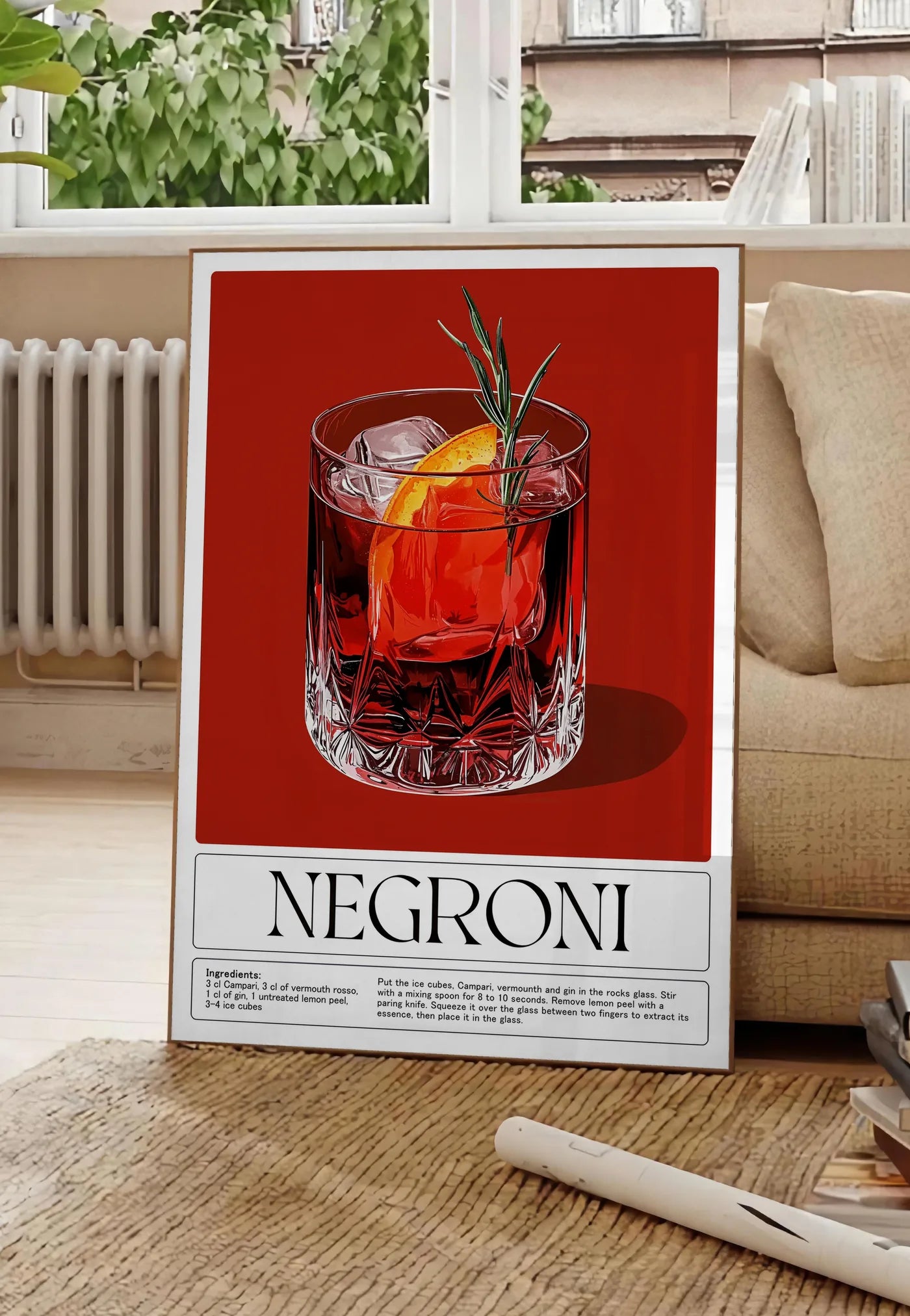 Poster affiche cocktail Negroni, posee au sol dans un salon parisien, devant une grande fenetre donnant sur un immeuble haussmannien, entre un ficus et un canape creme