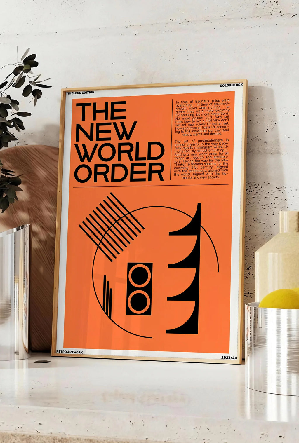 Affiche typographie The New World Order en noir sur orange, posee sur un plan de travail de cuisine en pierre claire, entre une branche d'eucalyptus en vase et un bocal de citrons