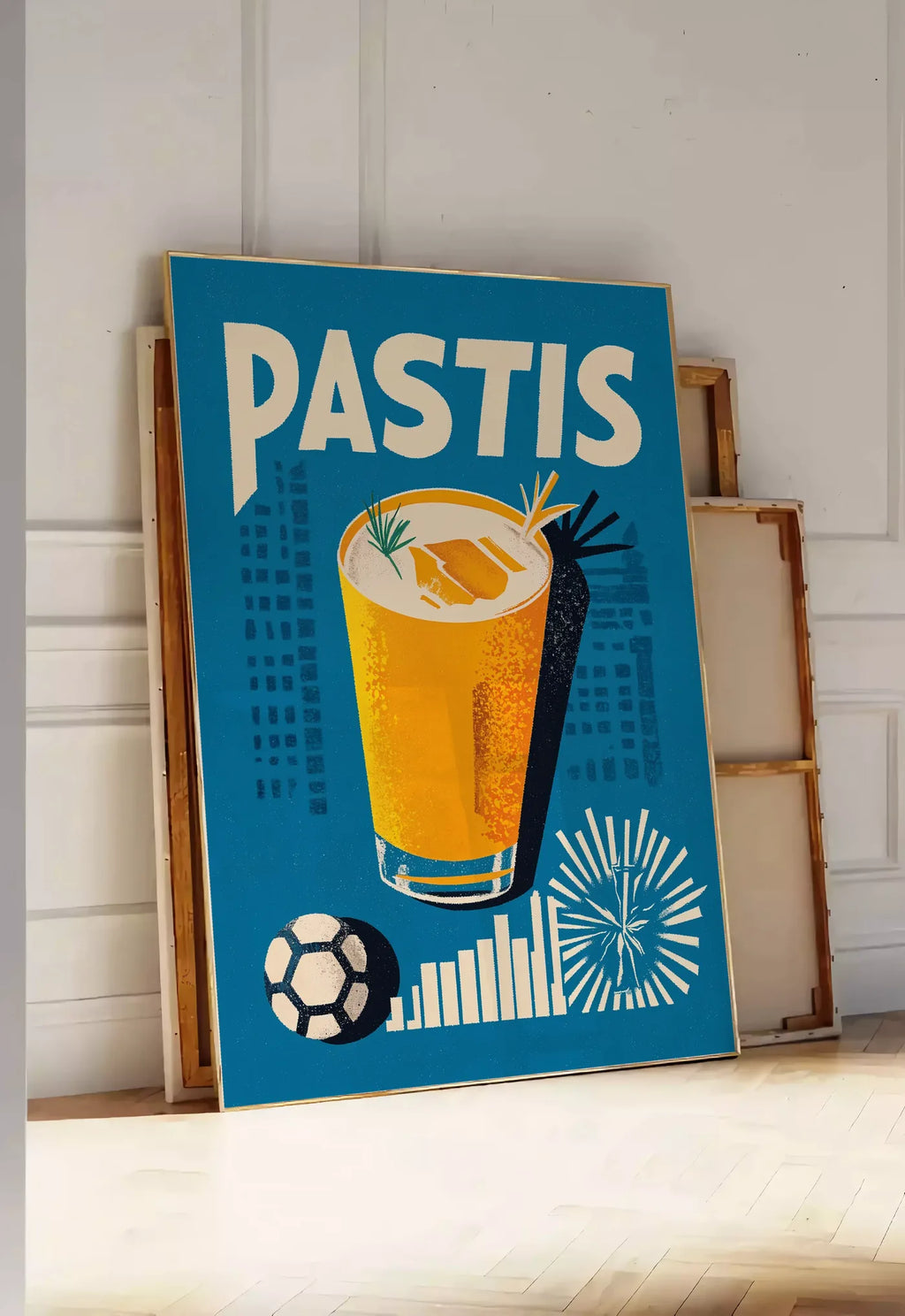 Tirage encadrable affiche cocktail Pastis Marseille, posee au sol dans une entree lumineuse, contre un mur a panneaux blancs, a cote de chassis en bois empiles