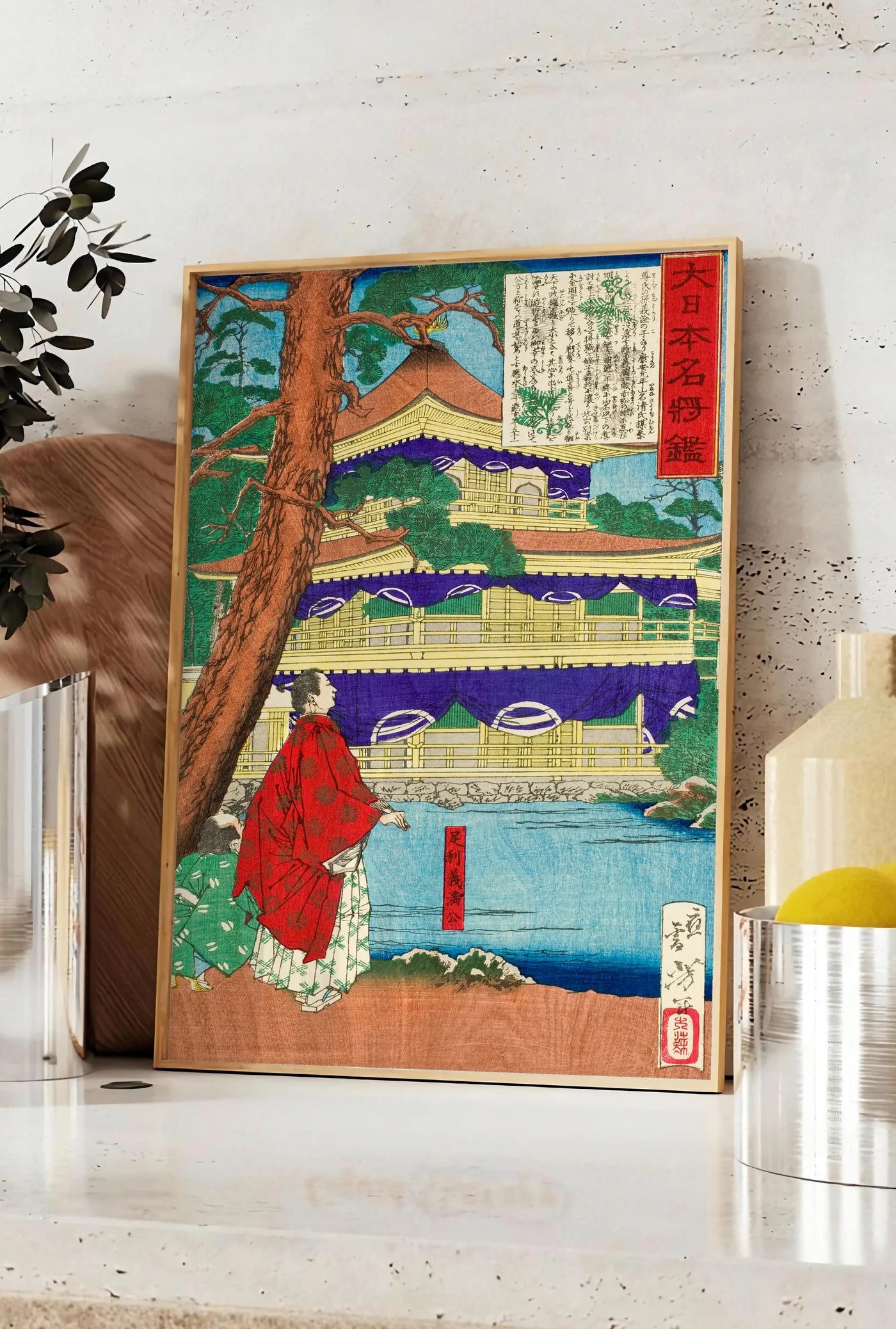 Affiche affiche pavillon dore et samurai art japonais, posee sur un plan de travail de cuisine en pierre claire, entre une branche d'eucalyptus en vase et un bocal de citrons