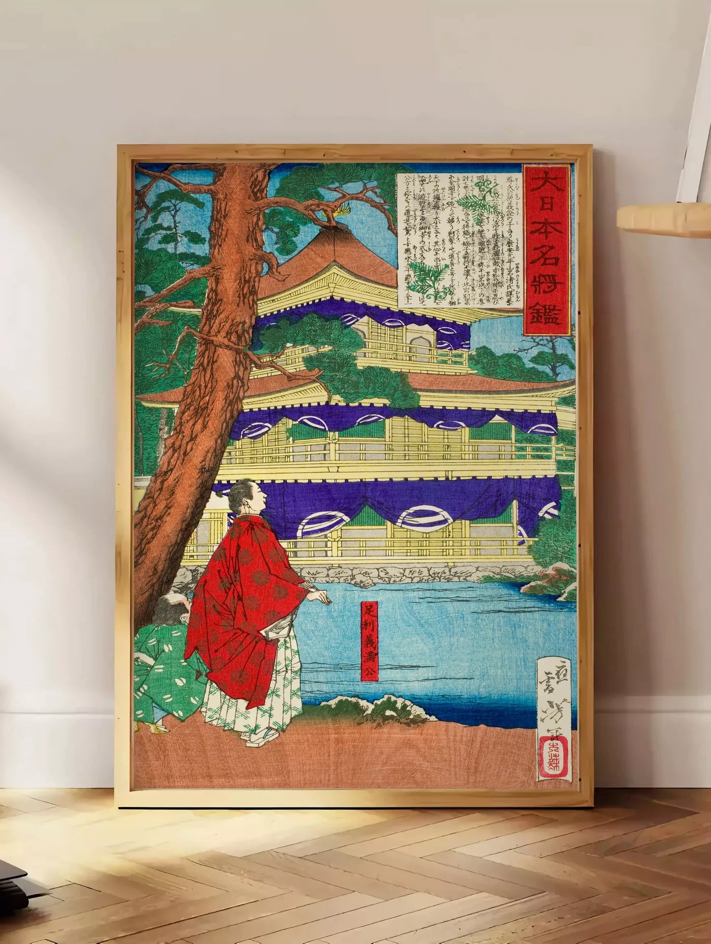 Estampe affiche pavillon dore et samurai art japonais, posee au sol dans un coin salon, sur un parquet a chevrons, pres d'une table d'appoint en chene chargee de livres