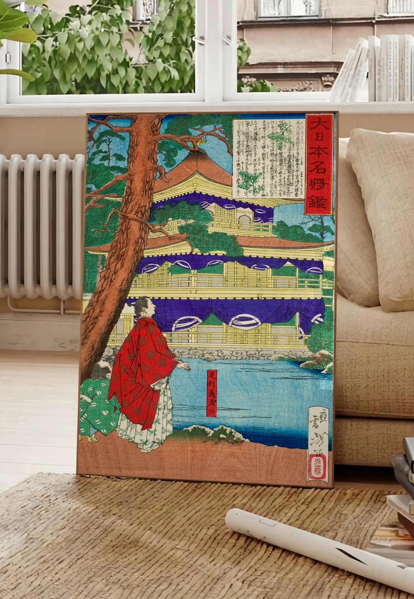 Poster affiche pavillon dore et samurai art japonais, posee au sol dans un salon parisien, devant une grande fenetre donnant sur un immeuble haussmannien, entre un ficus et un canape creme