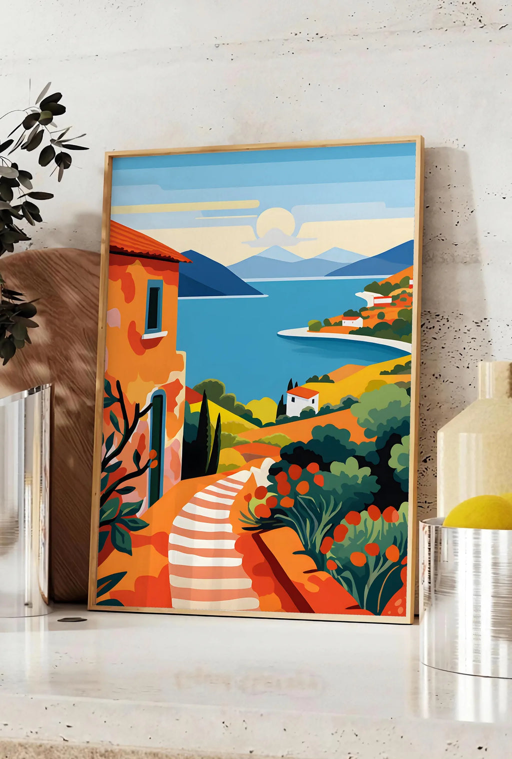 Affiche affiche paysage cote mediterranee, posee sur un plan de travail de cuisine en pierre claire, entre une branche d'eucalyptus en vase et un bocal de citrons