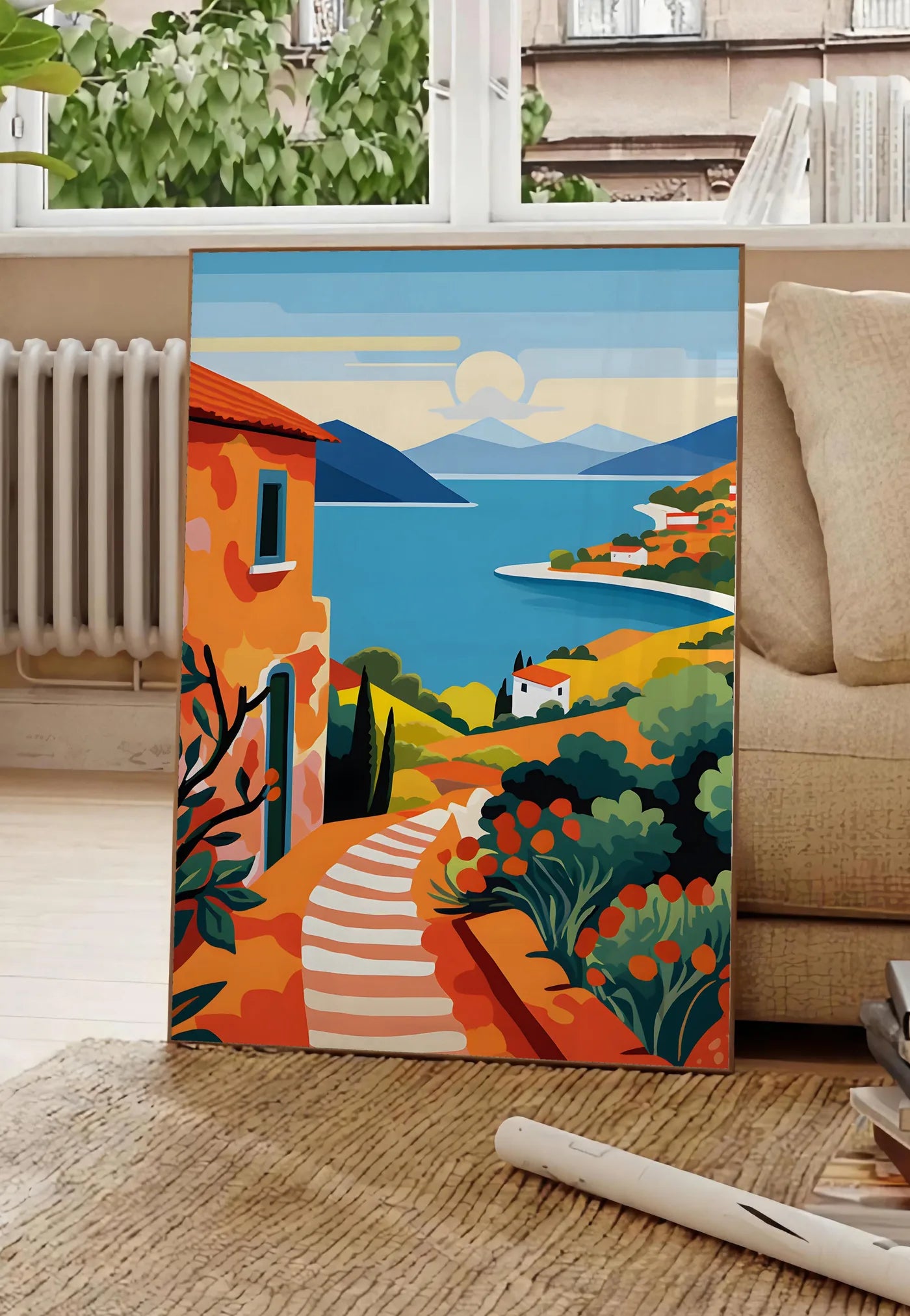 Poster affiche paysage cote mediterranee, posee au sol dans un salon parisien, devant une grande fenetre donnant sur un immeuble haussmannien, entre un ficus et un canape creme