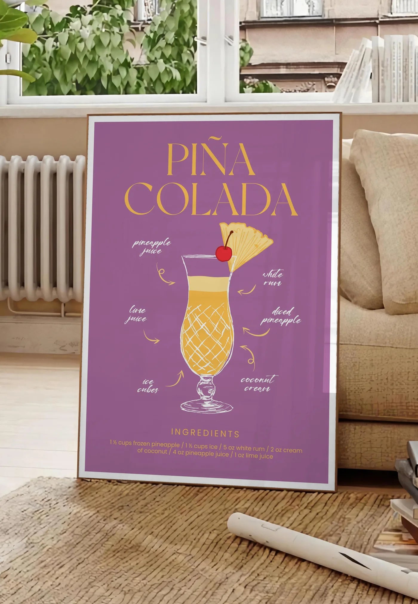 Poster affiche cocktail Pina Colada, posee au sol dans un salon parisien, devant une grande fenetre donnant sur un immeuble haussmannien, entre un ficus et un canape creme