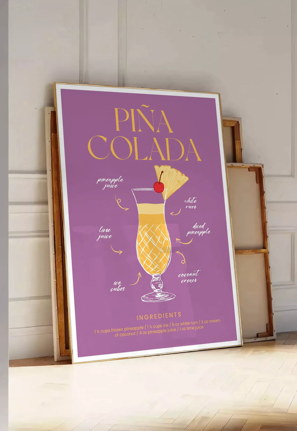 Tirage encadrable affiche cocktail Pina Colada, posee au sol dans une entree lumineuse, contre un mur a panneaux blancs, a cote de chassis en bois empiles