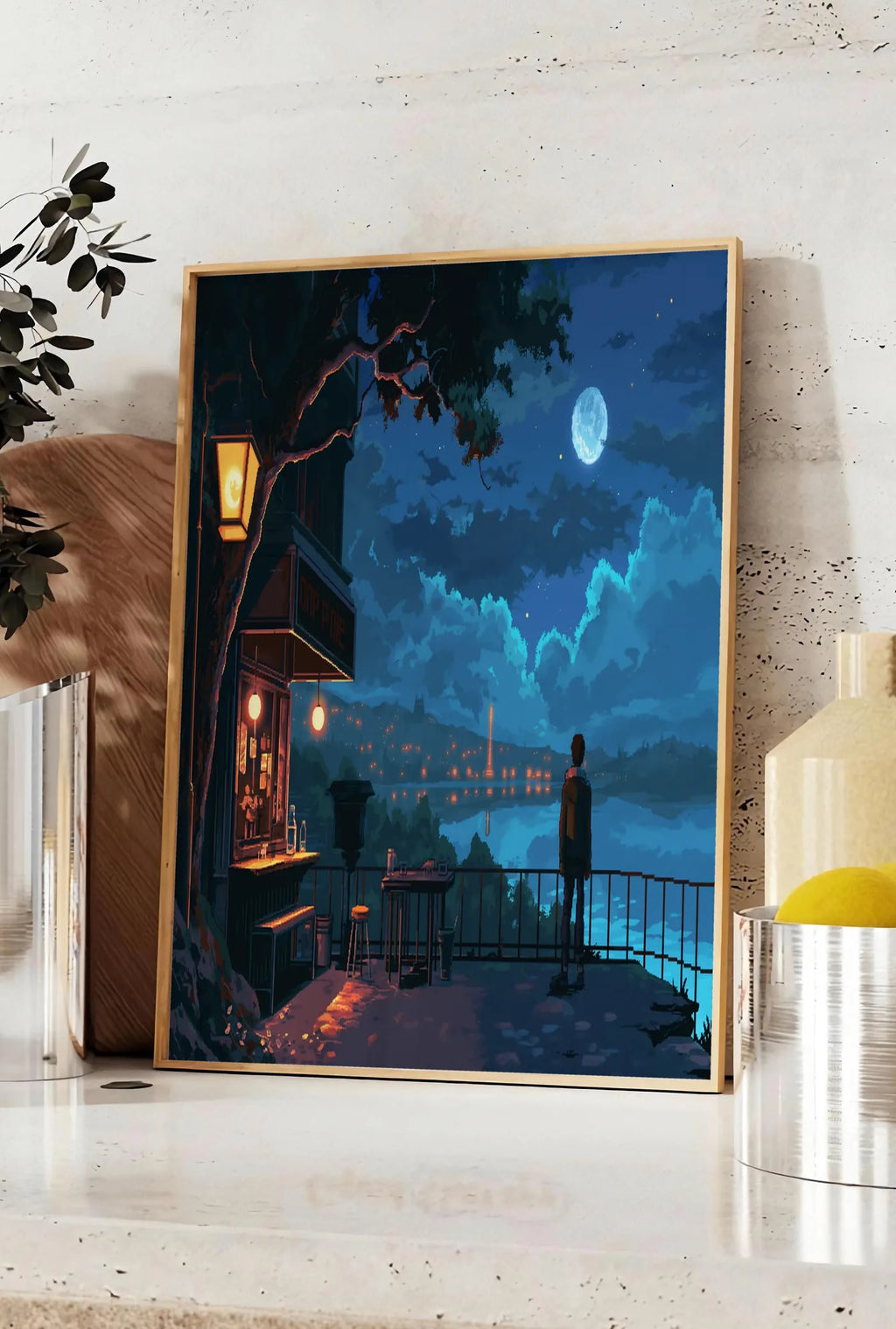 Affiche cafe de nuit pixel art, posee sur un plan de travail de cuisine en pierre claire, entre une branche d'eucalyptus en vase et un bocal de citrons