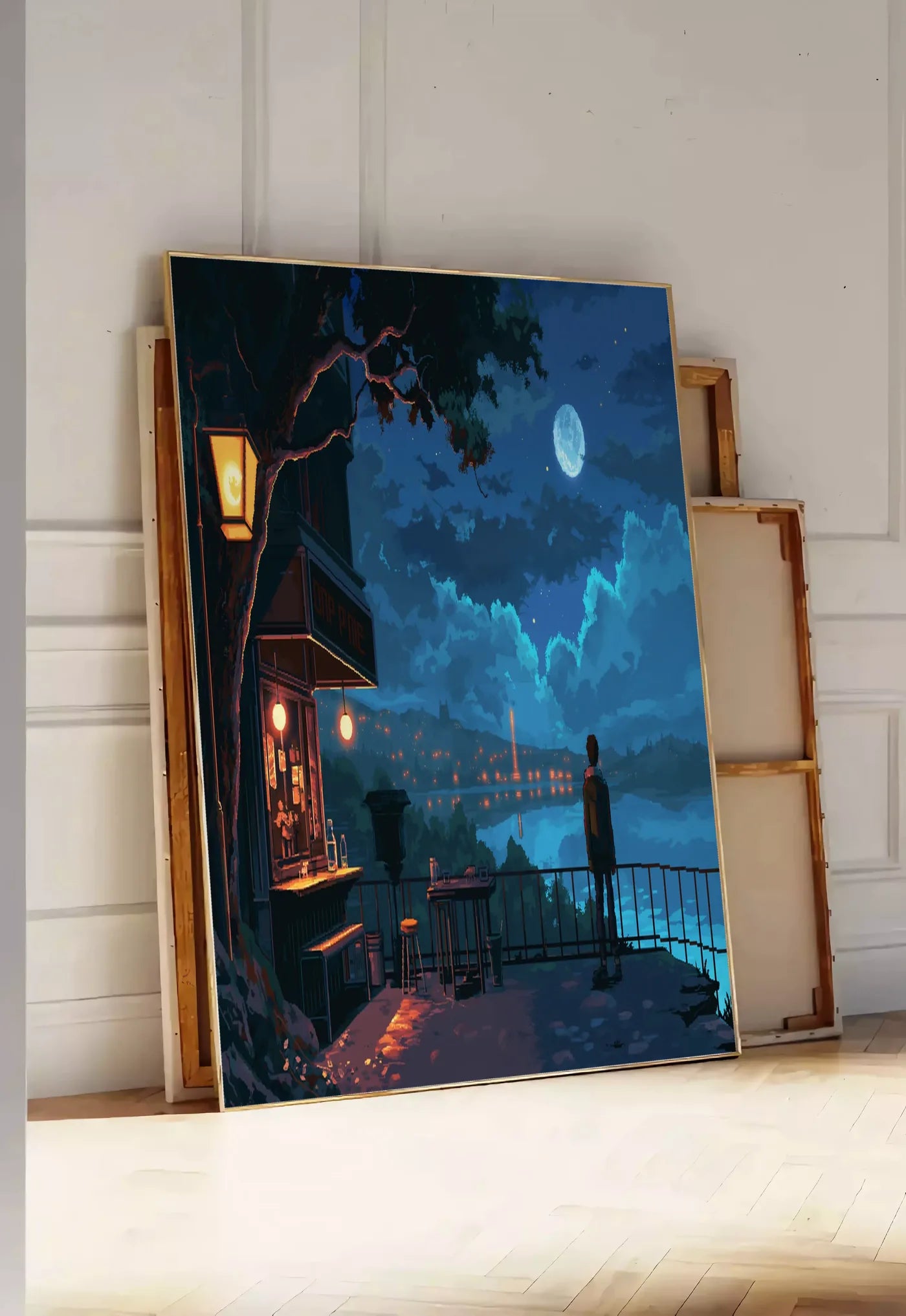 Tirage encadrable cafe de nuit pixel art, posee au sol dans une entree lumineuse, contre un mur a panneaux blancs, a cote de chassis en bois empiles