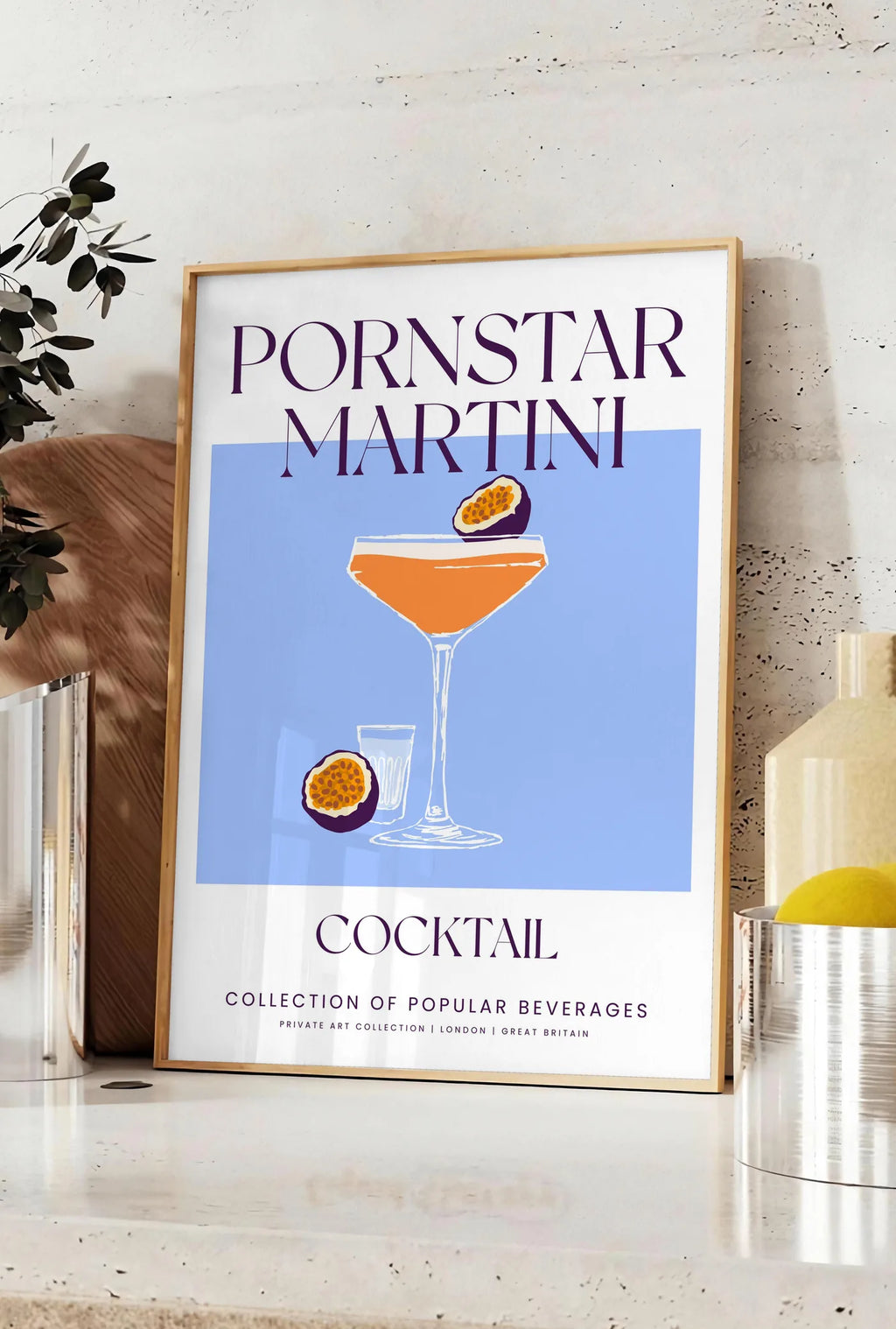 Affiche affiche cocktail Pornstar Martini, posee sur un plan de travail de cuisine en pierre claire, entre une branche d'eucalyptus en vase et un bocal de citrons