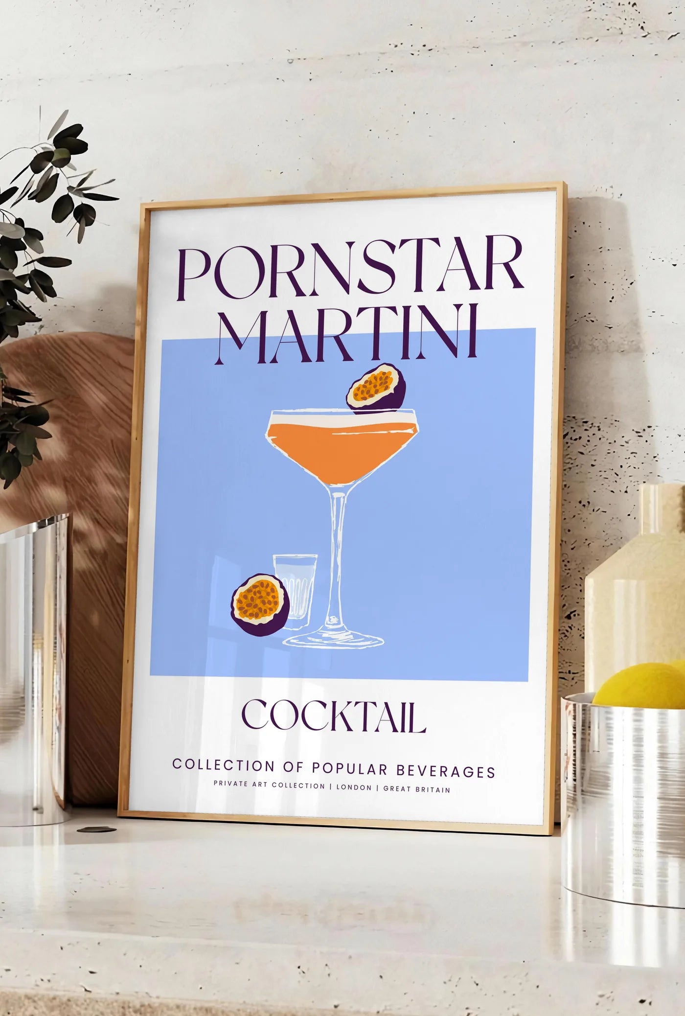 Affiche affiche cocktail Pornstar Martini, posee sur un plan de travail de cuisine en pierre claire, entre une branche d'eucalyptus en vase et un bocal de citrons