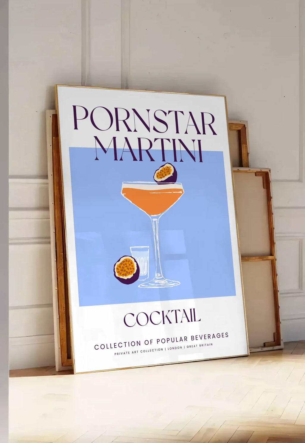Tirage encadrable affiche cocktail Pornstar Martini, posee au sol dans une entree lumineuse, contre un mur a panneaux blancs, a cote de chassis en bois empiles