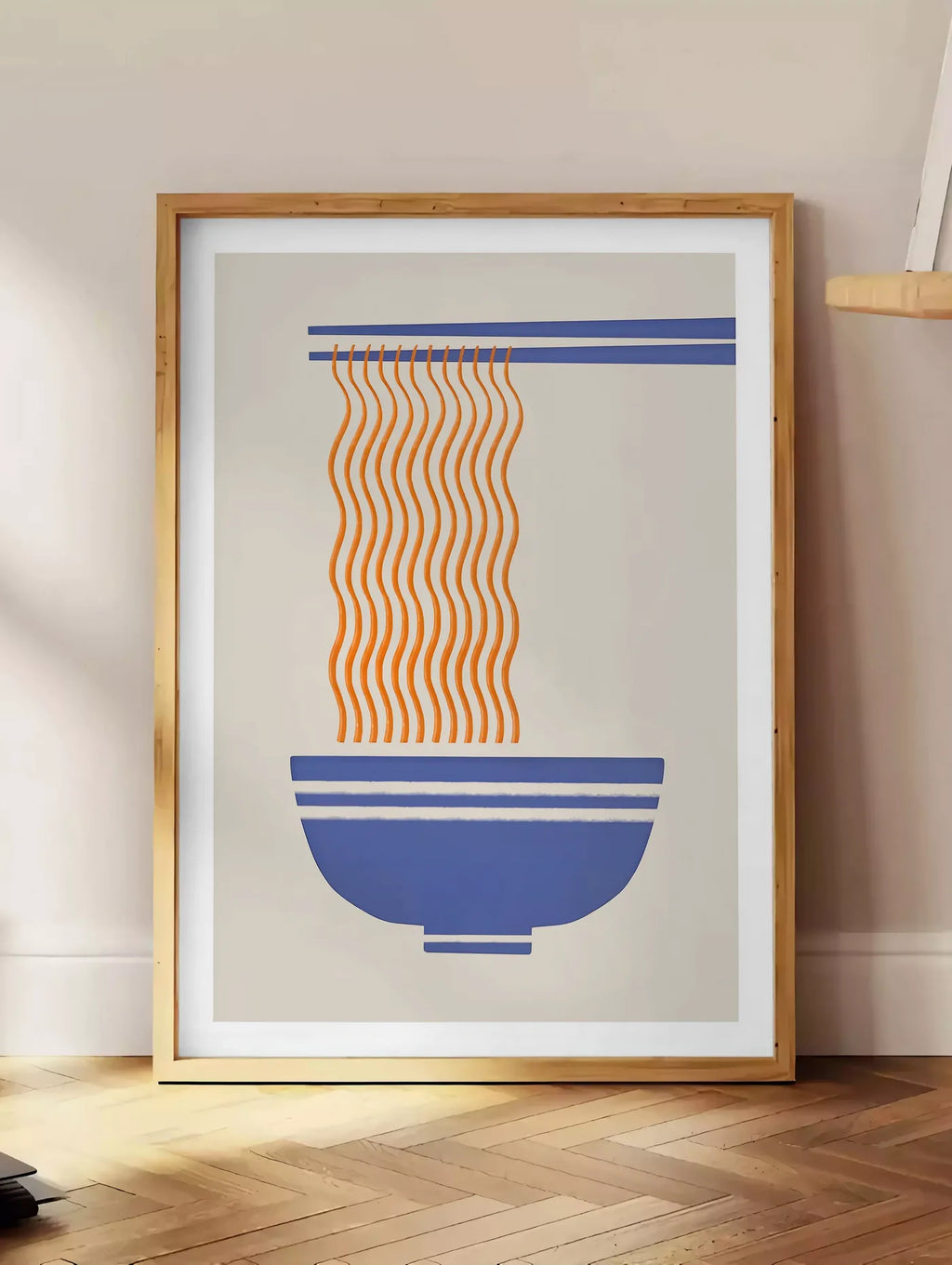 Estampe affiche cuisine ramen, posee au sol dans un coin salon, sur un parquet a chevrons, pres d'une table d'appoint en chene chargee de livres