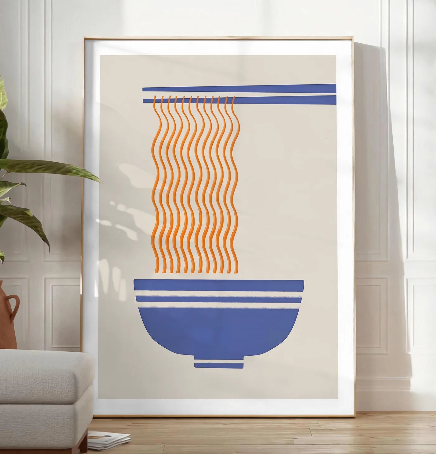 Reproduction affiche cuisine ramen, posee au sol dans un salon minimaliste clair, a cote d'un canape beige et d'une plante verte, sur un parquet clair