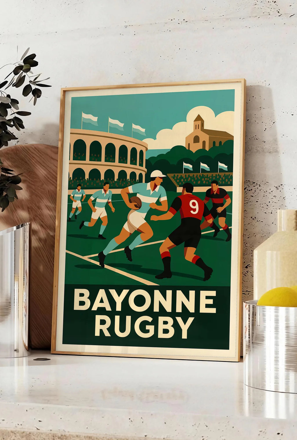 Affiche joueurs de rugby en maillots rayés, posee sur un plan de travail de cuisine en pierre claire, entre une branche d'eucalyptus en vase et un bocal de citrons