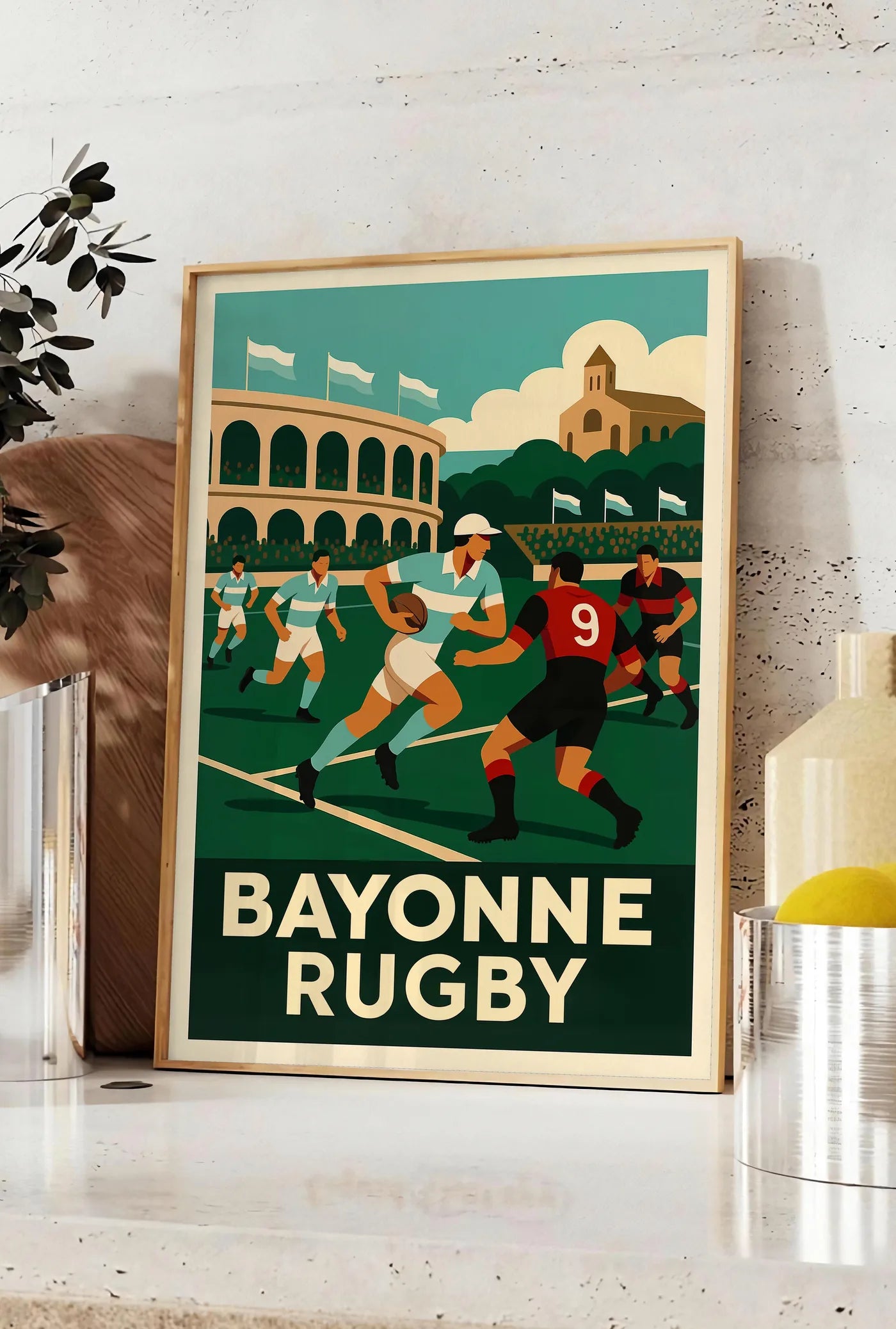 Affiche joueurs de rugby en maillots rayés, posee sur un plan de travail de cuisine en pierre claire, entre une branche d'eucalyptus en vase et un bocal de citrons