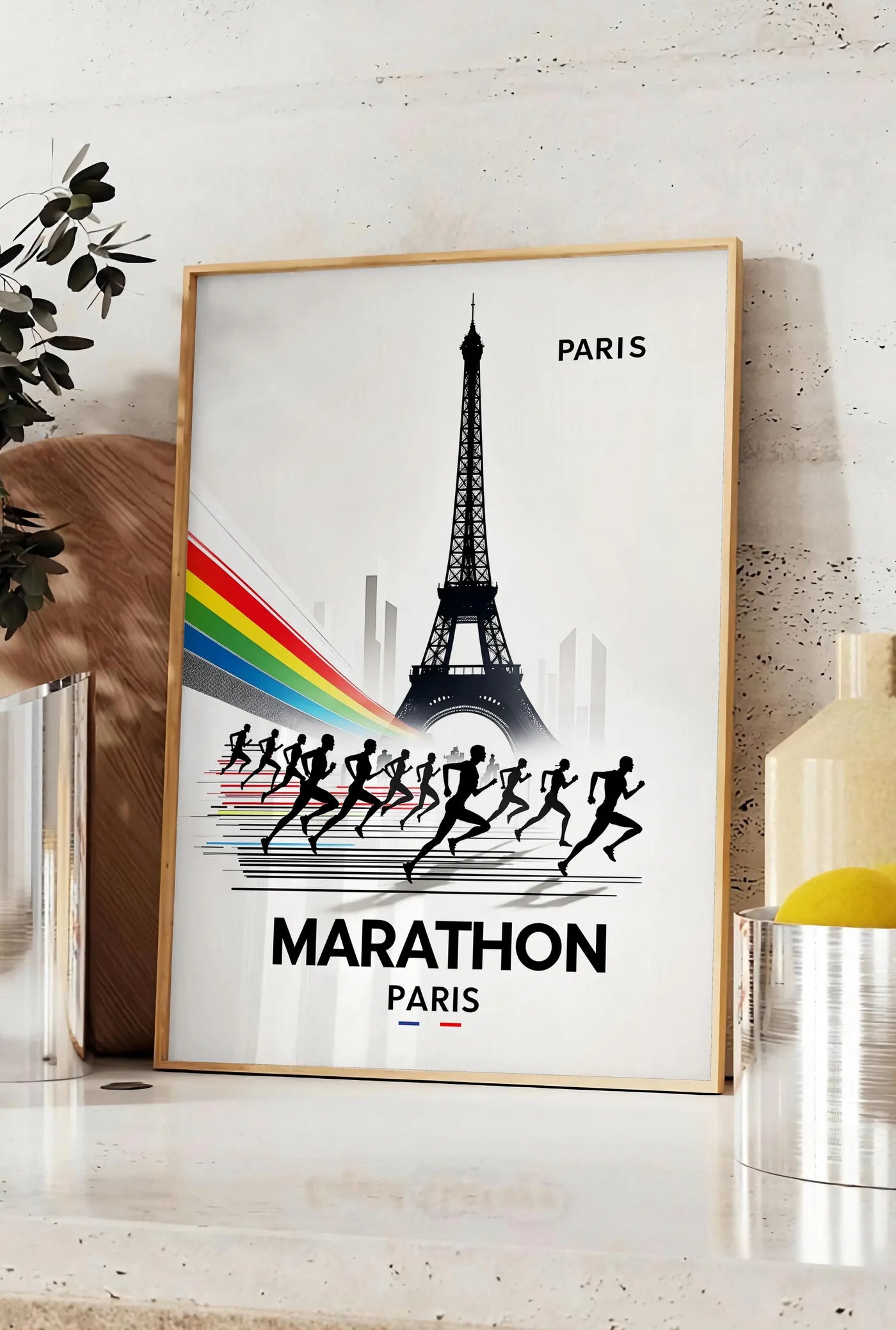 Affiche silhouettes de coureurs devant la Tour Eiffel, posee sur un plan de travail de cuisine en pierre claire, entre une branche d'eucalyptus en vase et un bocal de citrons
