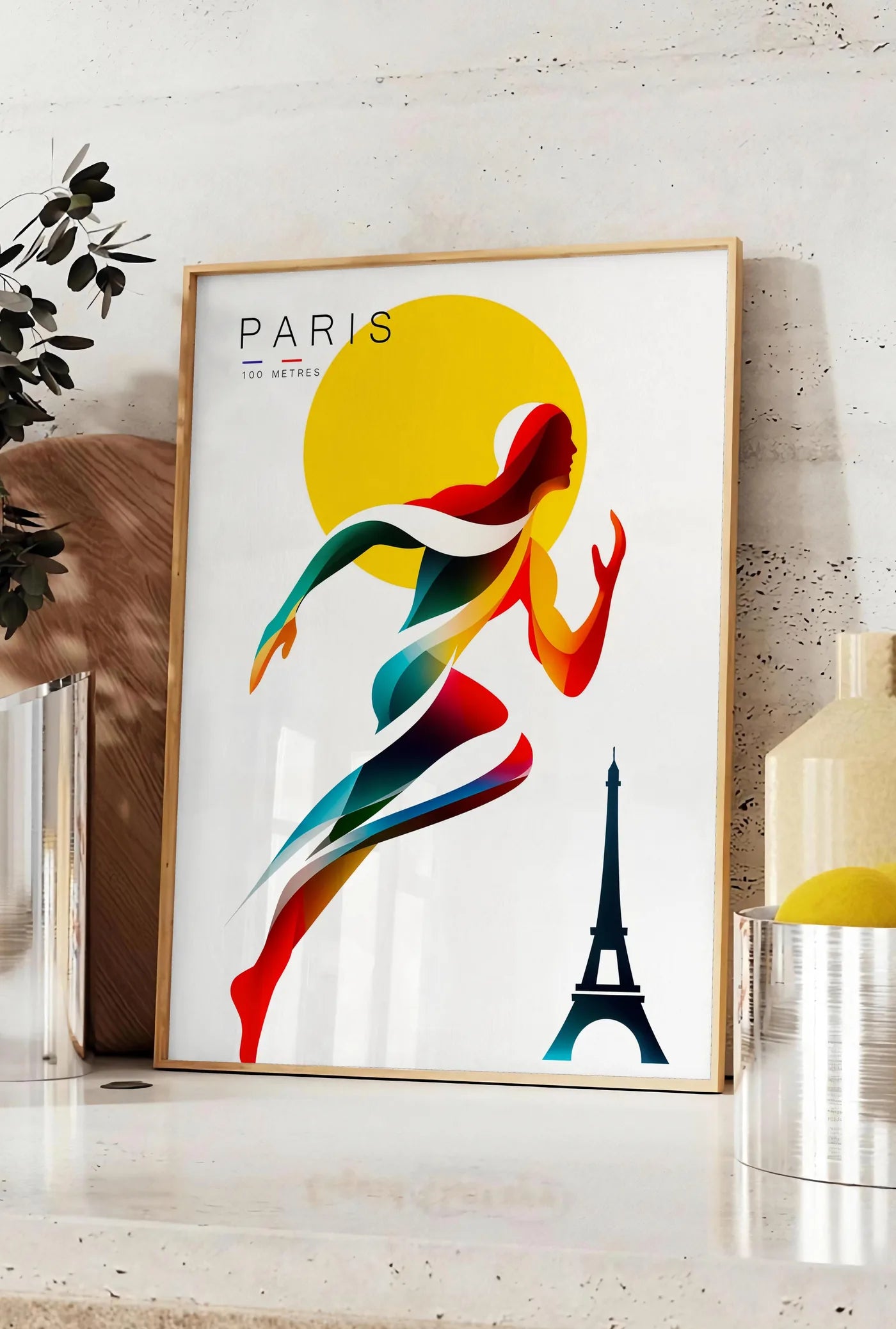 Affiche affiche Paris 100 metres, posee sur un plan de travail de cuisine en pierre claire, entre une branche d'eucalyptus en vase et un bocal de citrons
