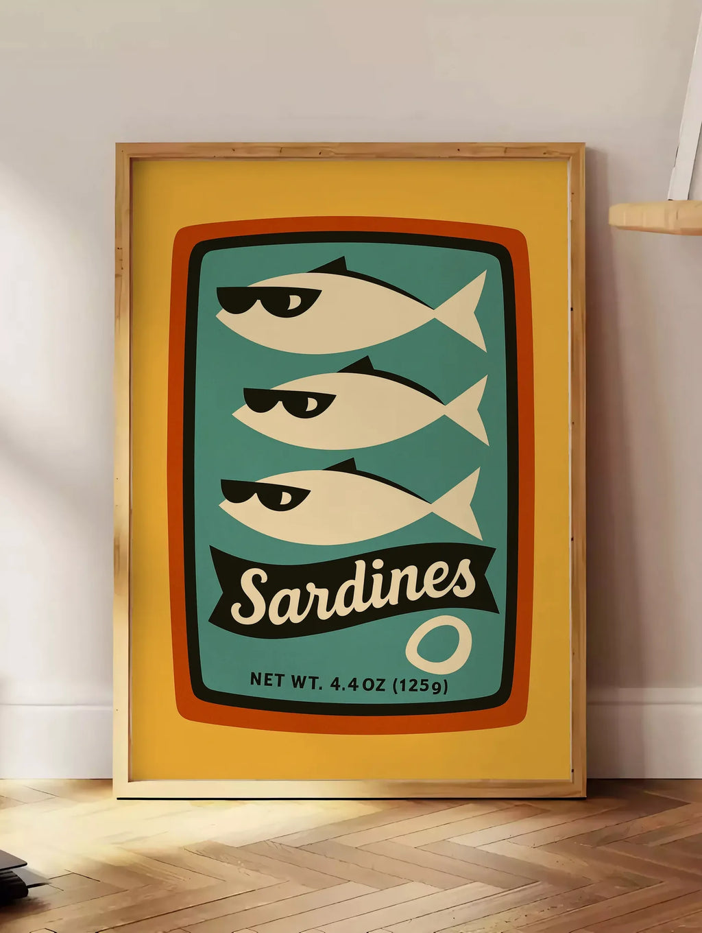 Estampe affiche cuisine sardines, posee au sol dans un coin salon, sur un parquet a chevrons, pres d'une table d'appoint en chene chargee de livres
