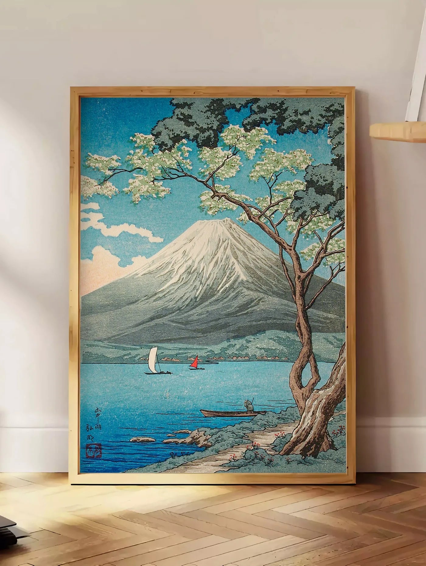 Estampe affiche Mont Fuji estampe, posee au sol dans un coin salon, sur un parquet a chevrons, pres d'une table d'appoint en chene chargee de livres