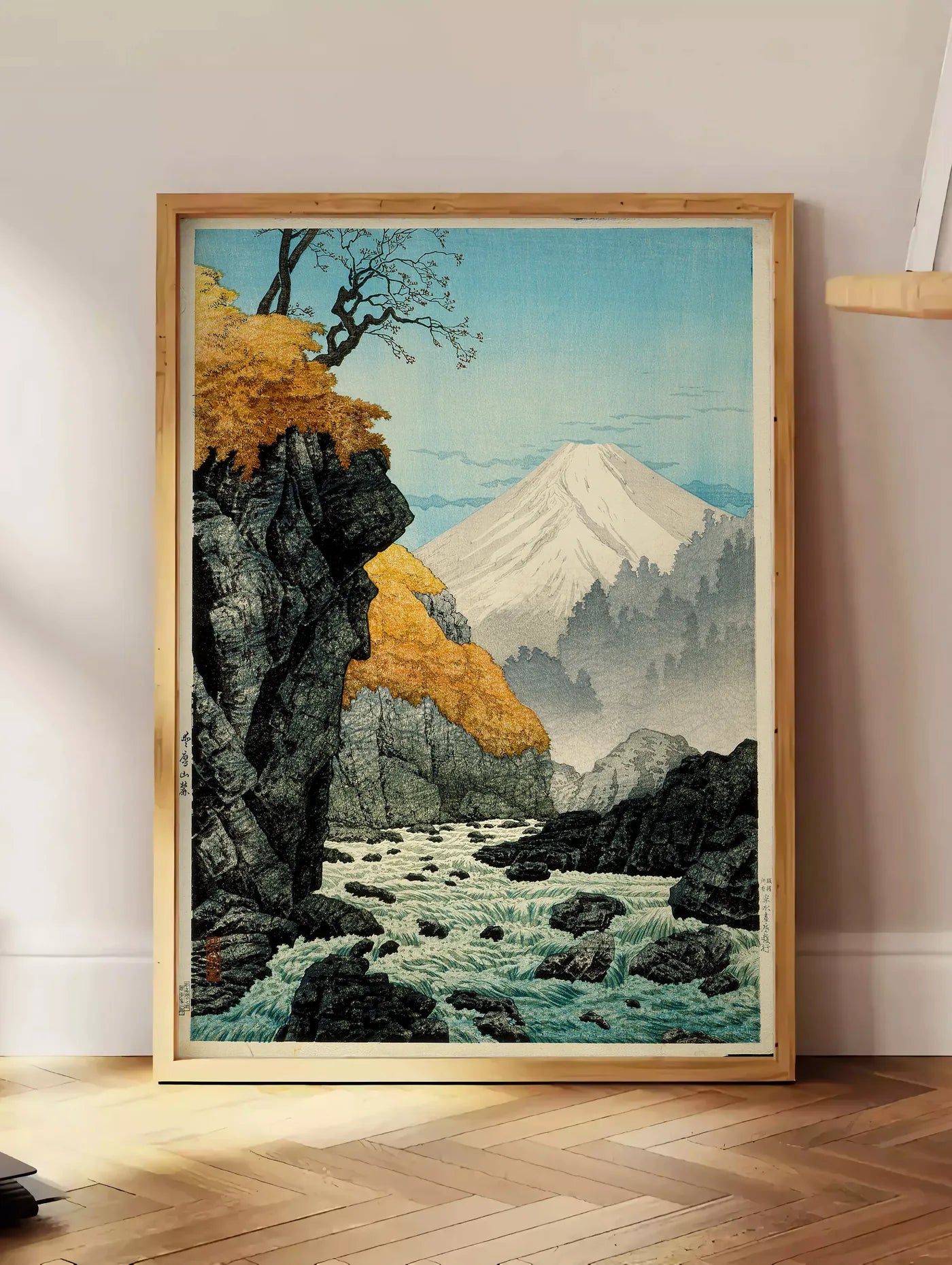 Estampe affiche Mont Fuji estampe, posee au sol dans un coin salon, sur un parquet a chevrons, pres d'une table d'appoint en chene chargee de livres