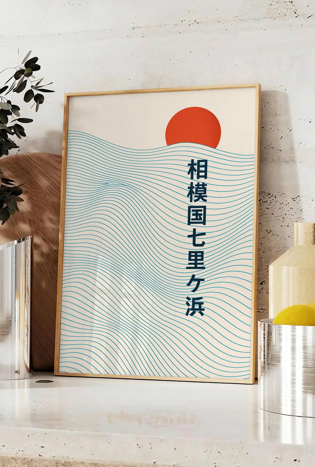 Affiche affiche soleil rouge levant au-dessus de vagues japonaises au trait, posee sur un plan de travail de cuisine en pierre claire, entre une branche d'eucalyptus en vase et un bocal de citrons