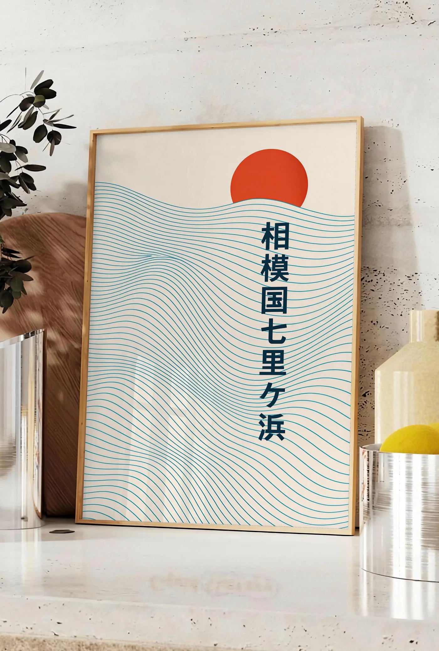 Affiche affiche soleil rouge levant au-dessus de vagues japonaises au trait, posee sur un plan de travail de cuisine en pierre claire, entre une branche d'eucalyptus en vase et un bocal de citrons