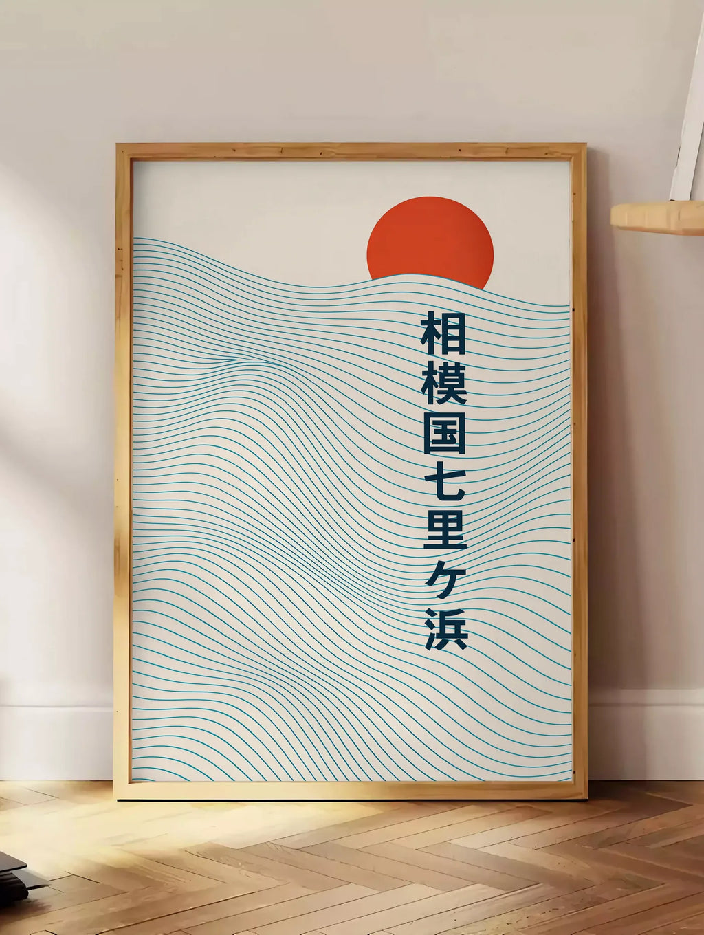 Estampe affiche soleil rouge levant au-dessus de vagues japonaises au trait, posee au sol dans un coin salon, sur un parquet a chevrons, pres d'une table d'appoint en chene chargee de livres