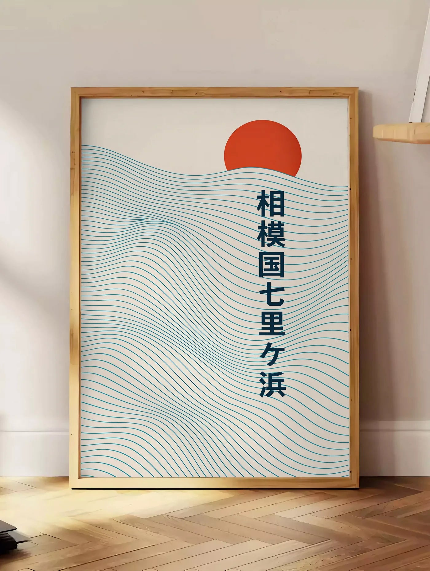 Estampe affiche soleil rouge levant au-dessus de vagues japonaises au trait, posee au sol dans un coin salon, sur un parquet a chevrons, pres d'une table d'appoint en chene chargee de livres