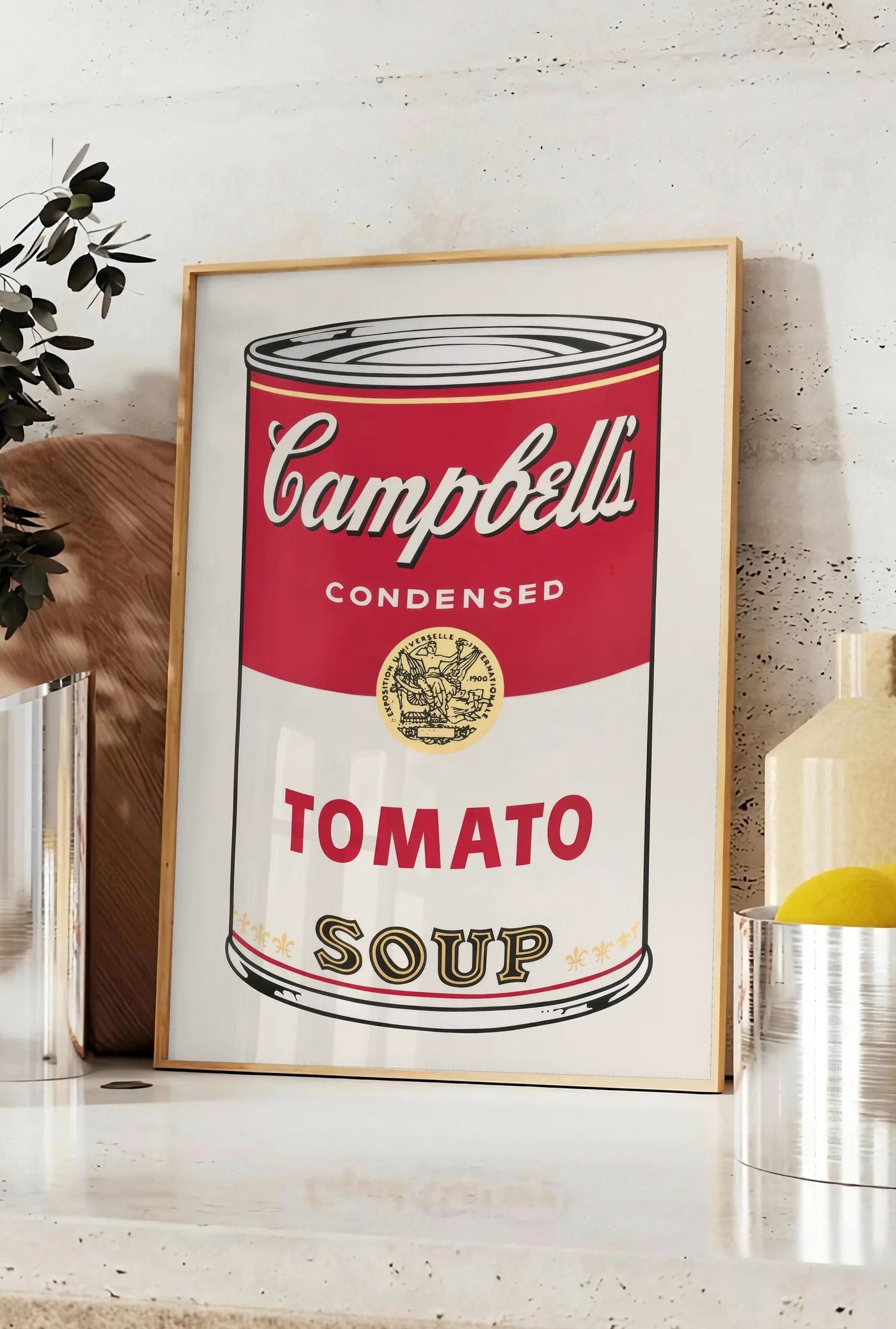 Affiche affiche cuisine soupe tomate, posee sur un plan de travail de cuisine en pierre claire, entre une branche d'eucalyptus en vase et un bocal de citrons