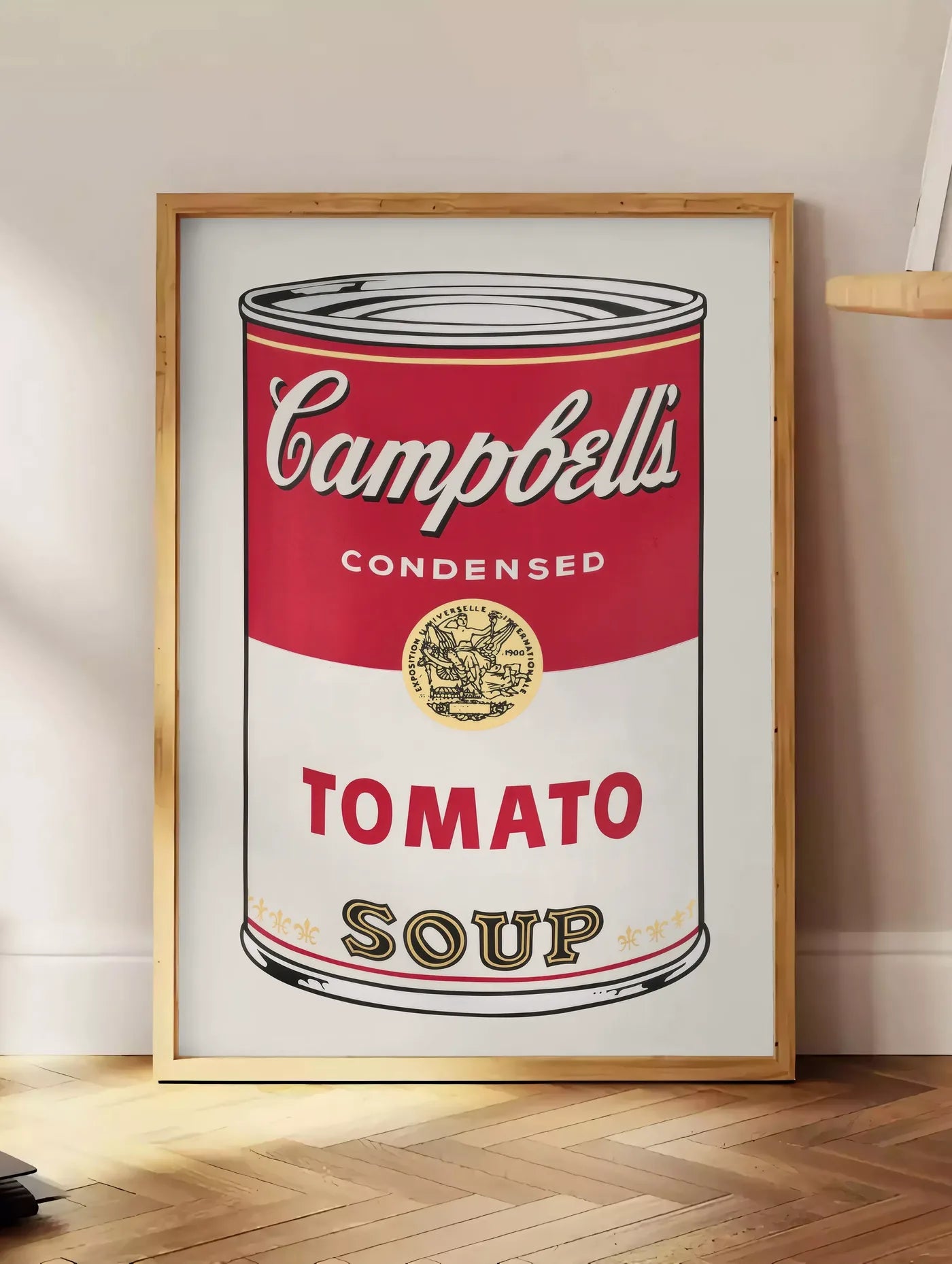 Estampe affiche cuisine soupe tomate, posee au sol dans un coin salon, sur un parquet a chevrons, pres d'une table d'appoint en chene chargee de livres