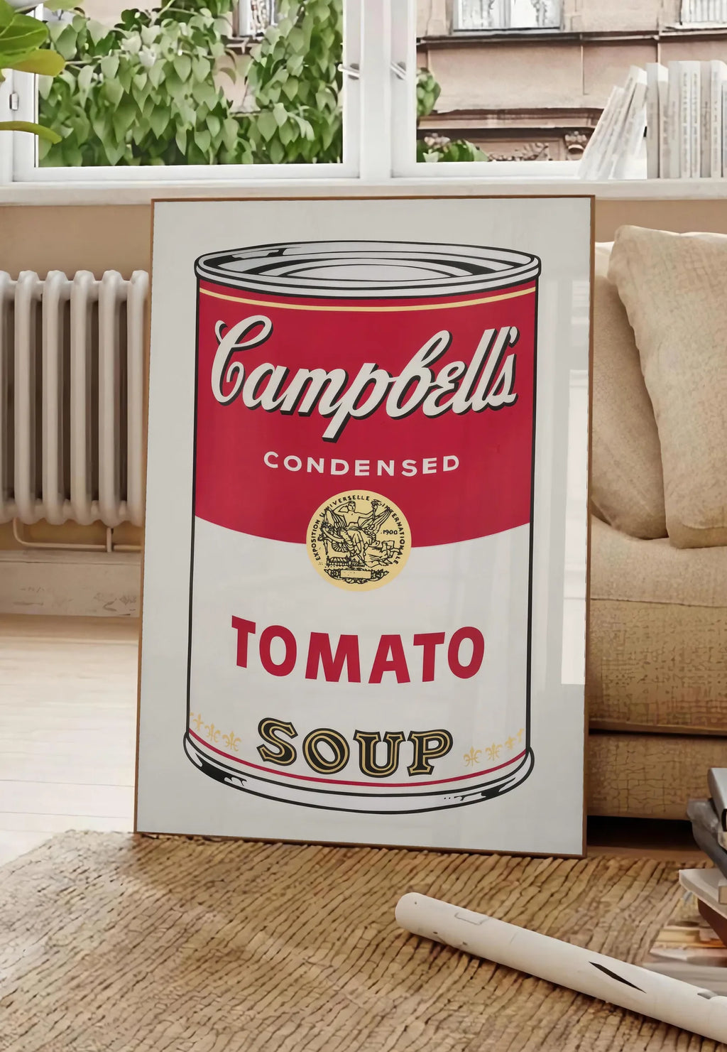 Poster affiche cuisine soupe tomate, posee au sol dans un salon parisien, devant une grande fenetre donnant sur un immeuble haussmannien, entre un ficus et un canape creme