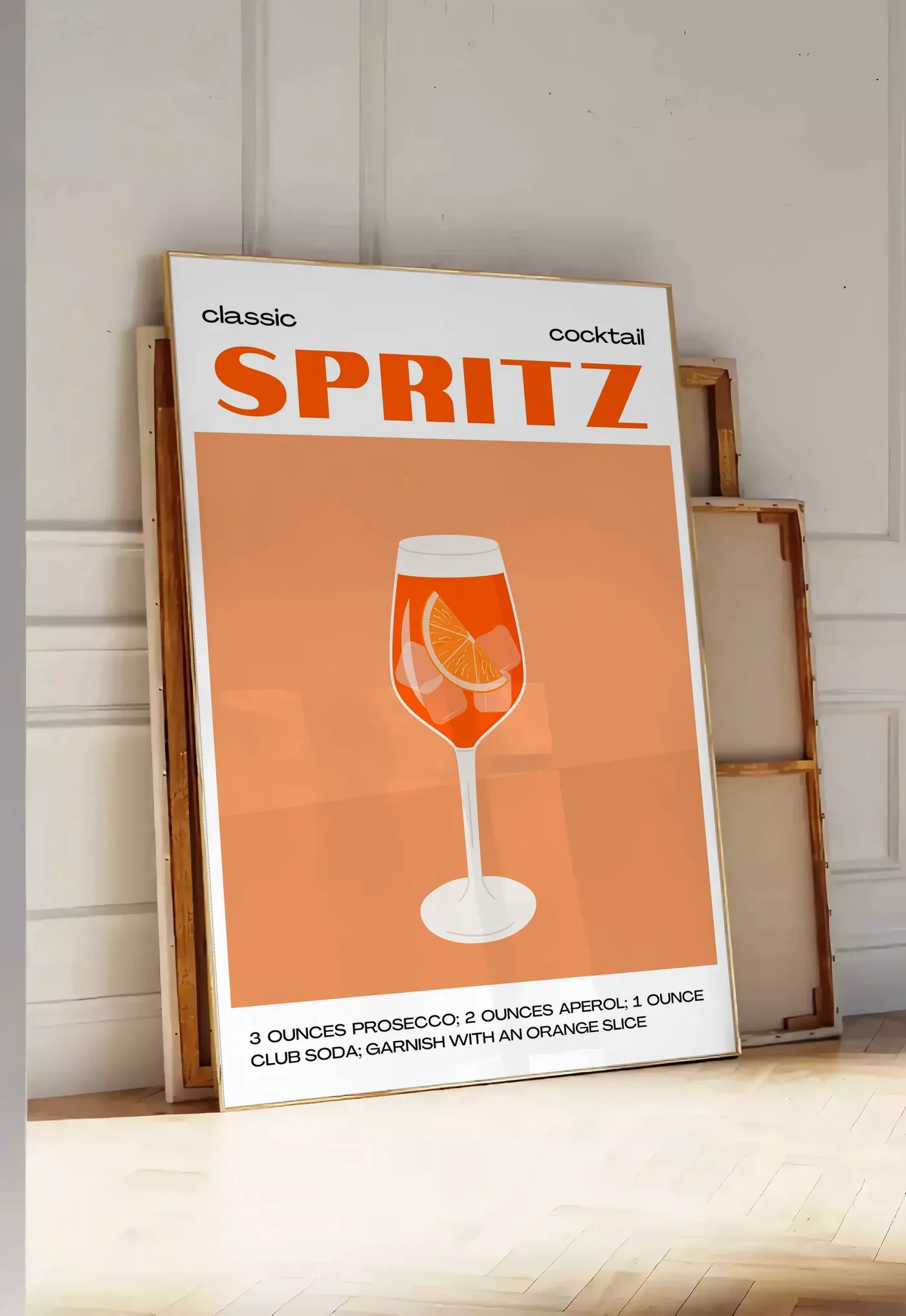 Tirage encadrable affiche cocktail Spritz, posee au sol dans une entree lumineuse, contre un mur a panneaux blancs, a cote de chassis en bois empiles