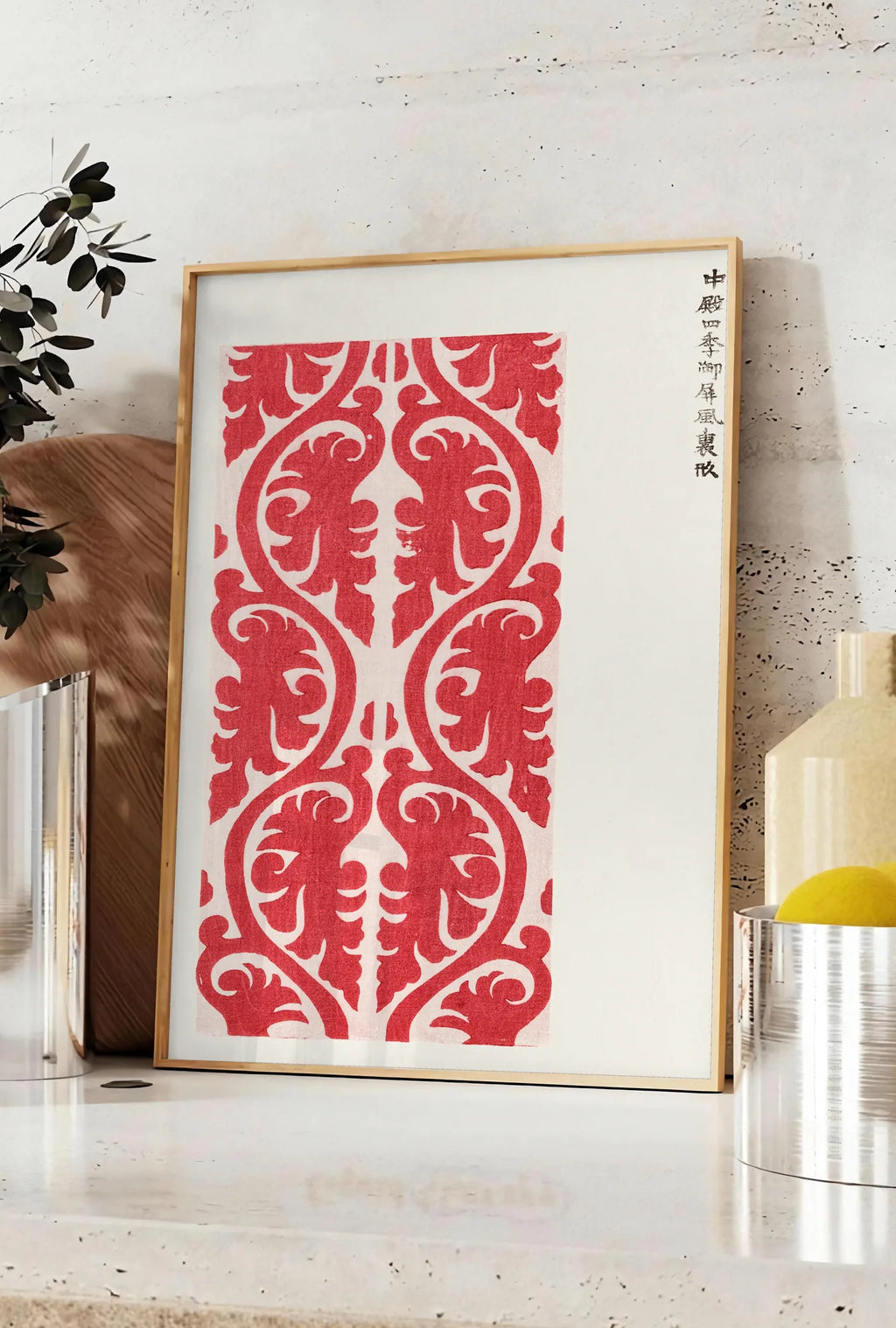 Affiche affiche motif rouge de feuillage de Taguchi Tomoki, posee sur un plan de travail de cuisine en pierre claire, entre une branche d'eucalyptus en vase et un bocal de citrons