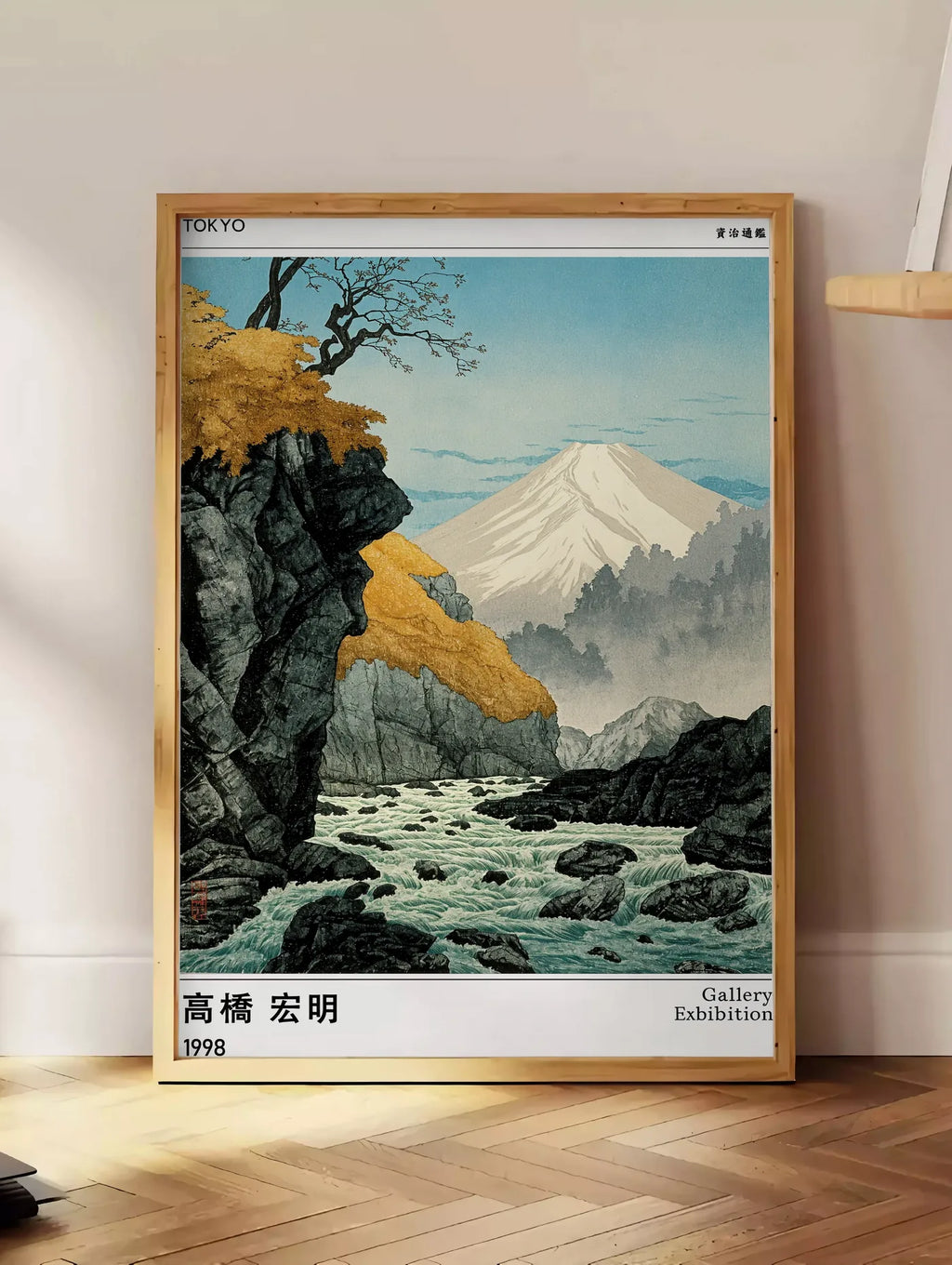 Estampe affiche mont Fuji Takahashi Hiroaki, posee au sol dans un coin salon, sur un parquet a chevrons, pres d'une table d'appoint en chene chargee de livres