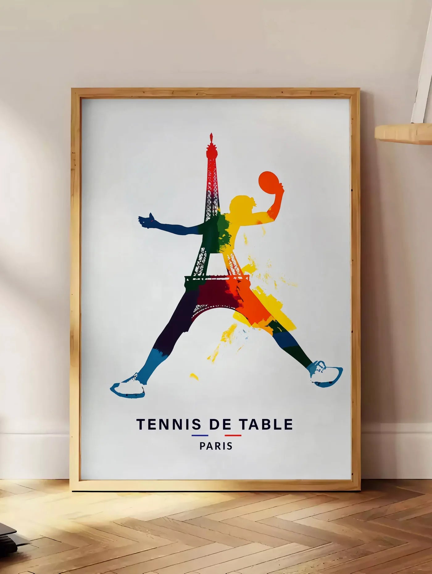 Estampe joueur de tennis de table bondissant, posee au sol dans un coin salon, sur un parquet a chevrons, pres d'une table d'appoint en chene chargee de livres