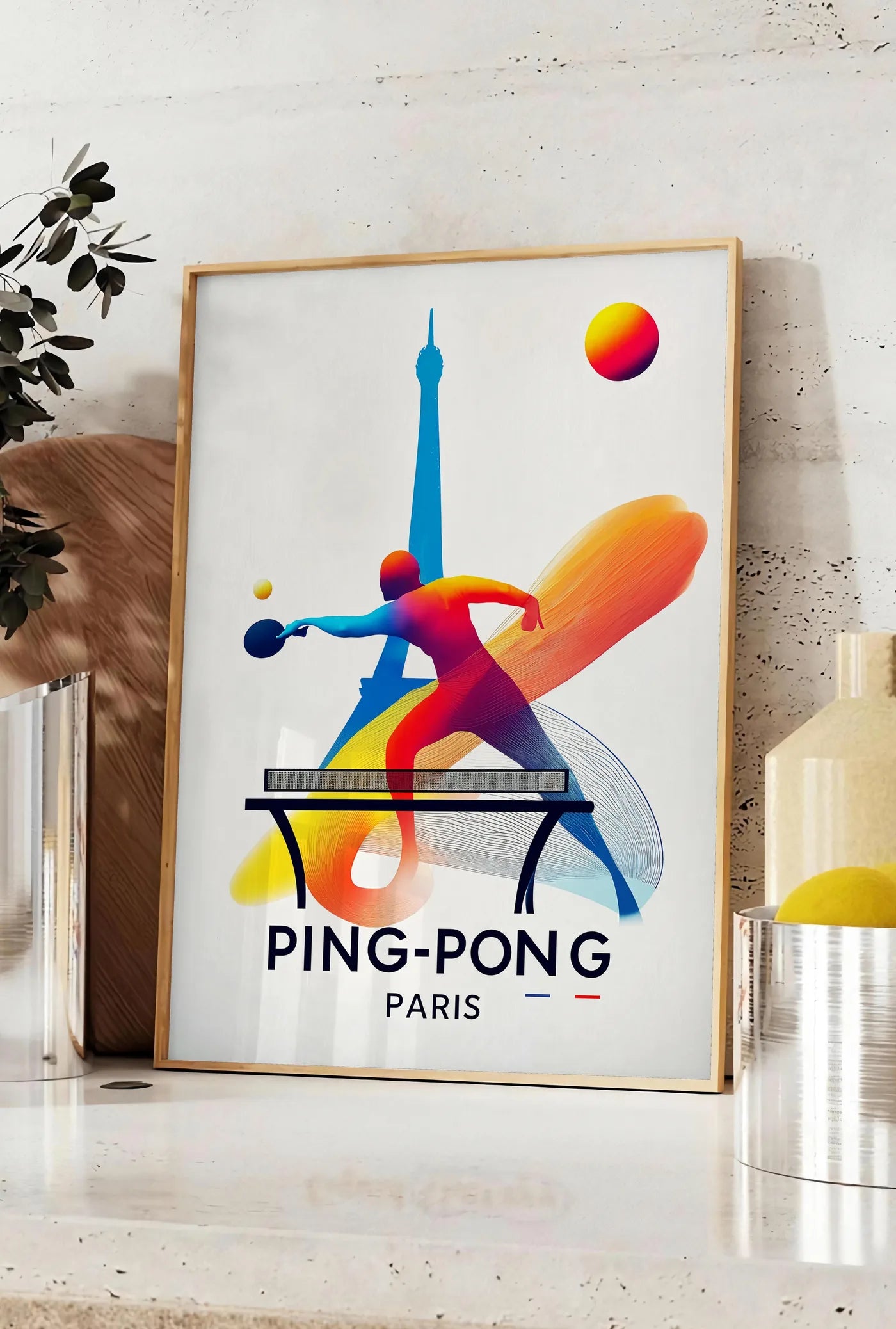 Affiche joueur de ping-pong en extension a la raquette, posee sur un plan de travail de cuisine en pierre claire, entre une branche d'eucalyptus en vase et un bocal de citrons