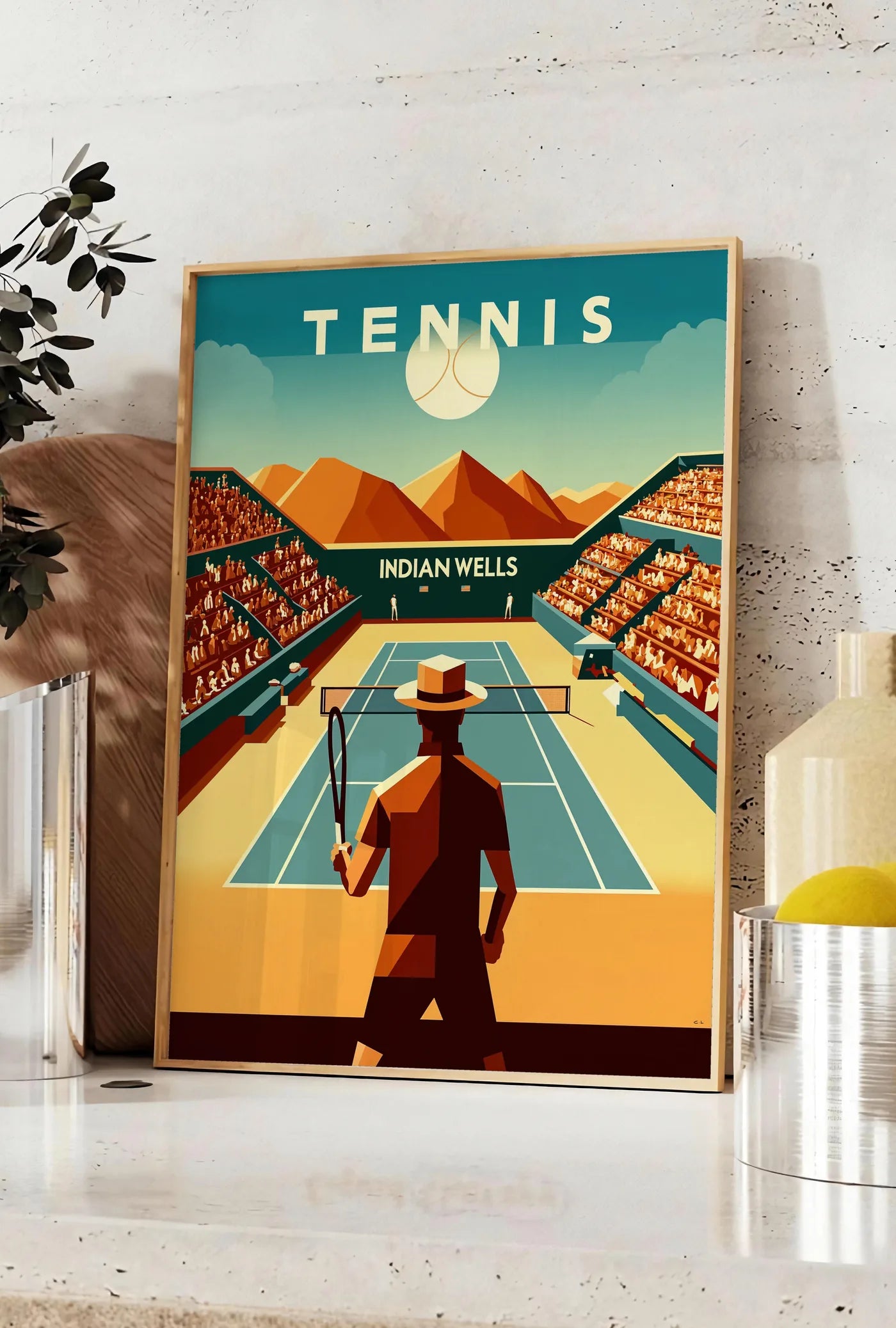 Affiche joueur de tennis face au court d'Indian Wells, posee sur un plan de travail de cuisine en pierre claire, entre une branche d'eucalyptus en vase et un bocal de citrons