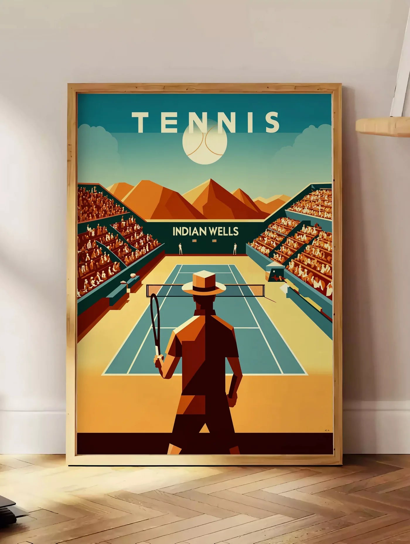 Estampe joueur de tennis face au court d'Indian Wells, posee au sol dans un coin salon, sur un parquet a chevrons, pres d'une table d'appoint en chene chargee de livres