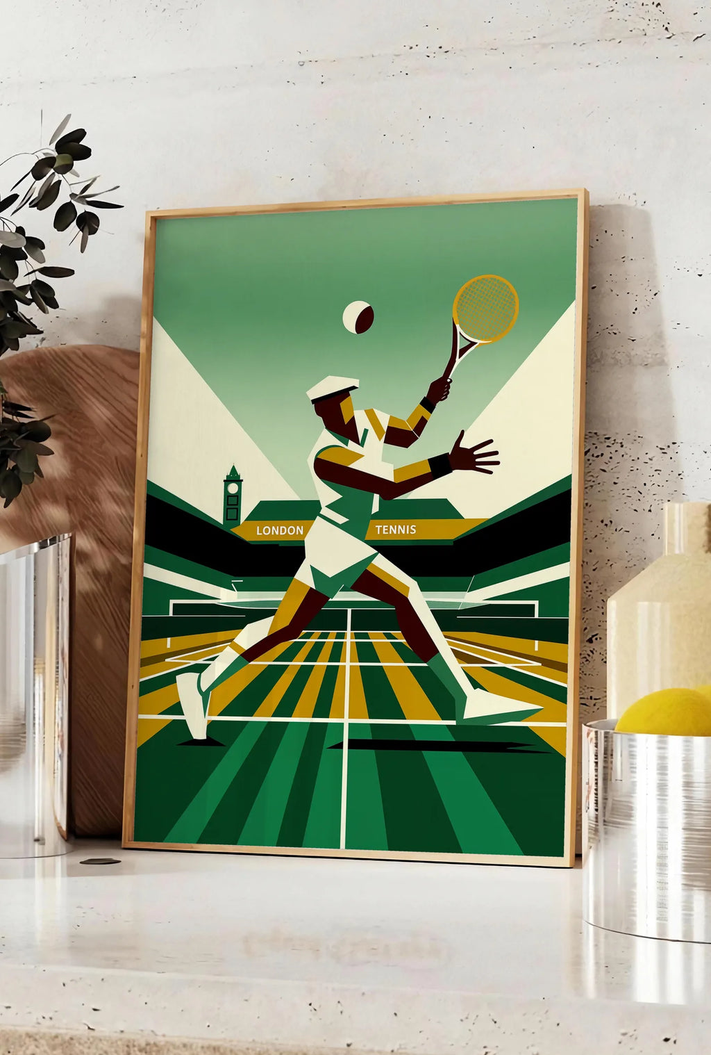 Affiche stylised tennis player serving with ocre yellow banner and black ivory stands, posee sur un plan de travail de cuisine en pierre claire, entre une branche d'eucalyptus en vase et un bocal de citrons