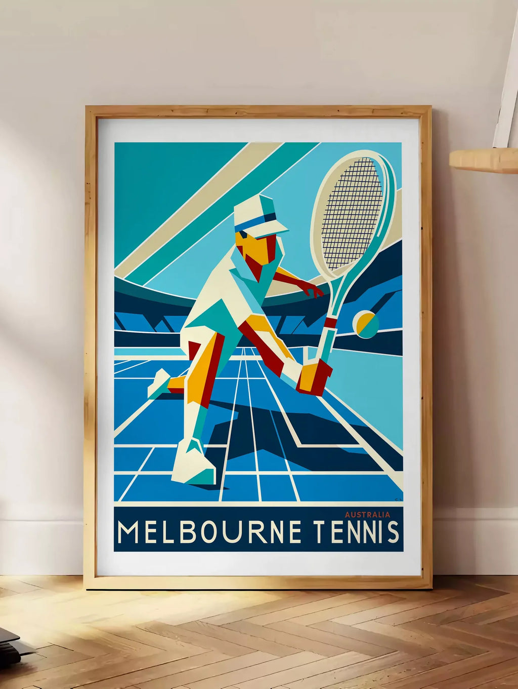 Estampe affiche tennis Melbourne Art Deco, posee au sol dans un coin salon, sur un parquet a chevrons, pres d'une table d'appoint en chene chargee de livres