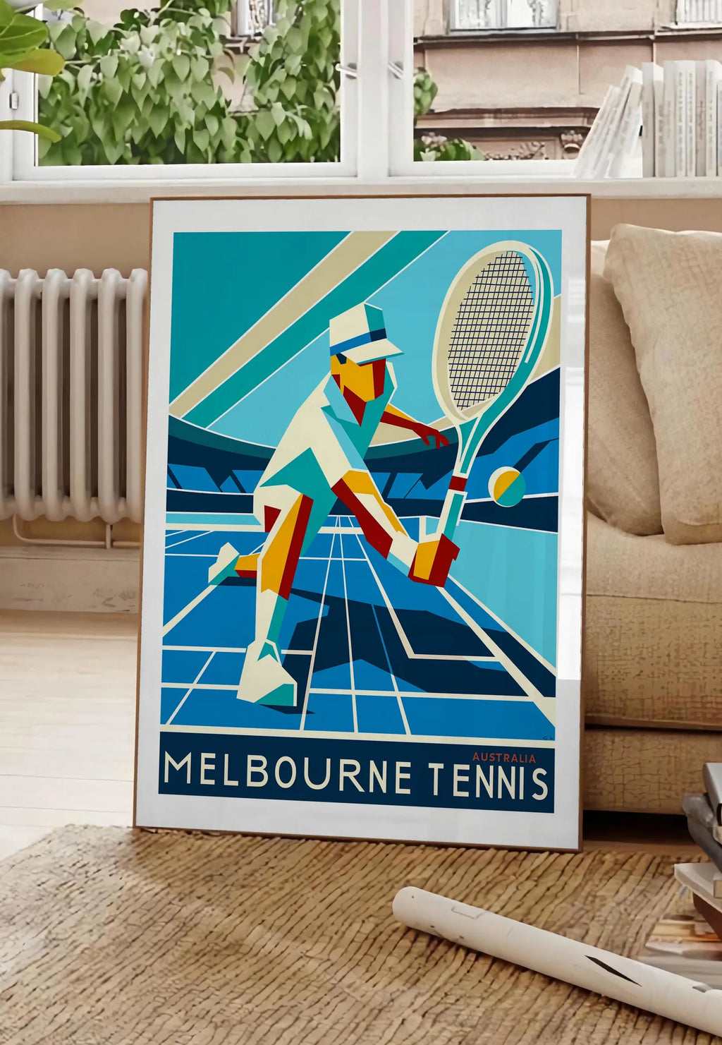 Poster affiche tennis Melbourne Art Deco, posee au sol dans un salon parisien, devant une grande fenetre donnant sur un immeuble haussmannien, entre un ficus et un canape creme