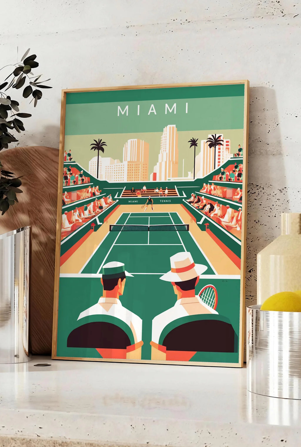 Affiche court de tennis vert et spectateurs, posee sur un plan de travail de cuisine en pierre claire, entre une branche d'eucalyptus en vase et un bocal de citrons