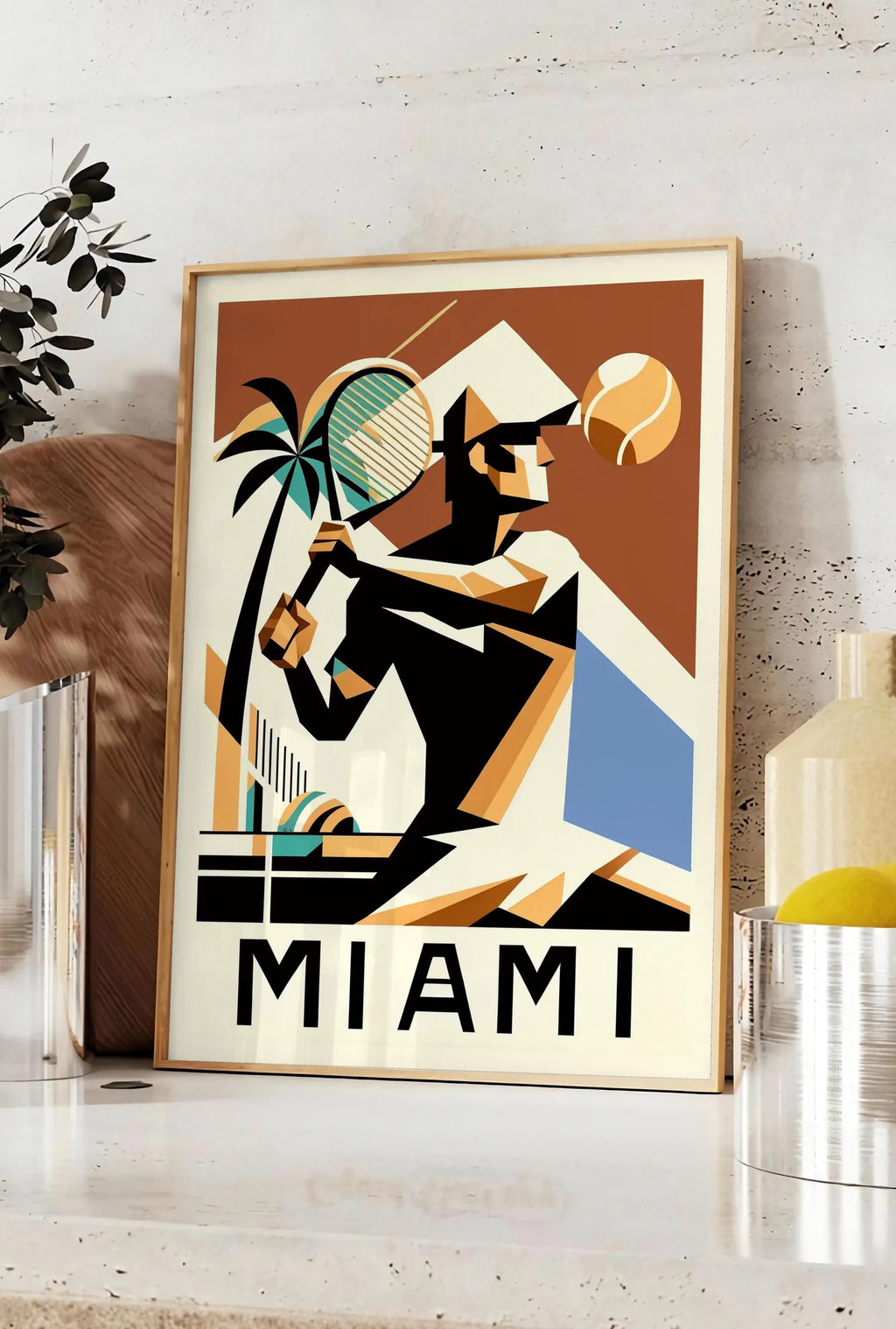 Affiche joueur de tennis cubiste a la raquette, posee sur un plan de travail de cuisine en pierre claire, entre une branche d'eucalyptus en vase et un bocal de citrons